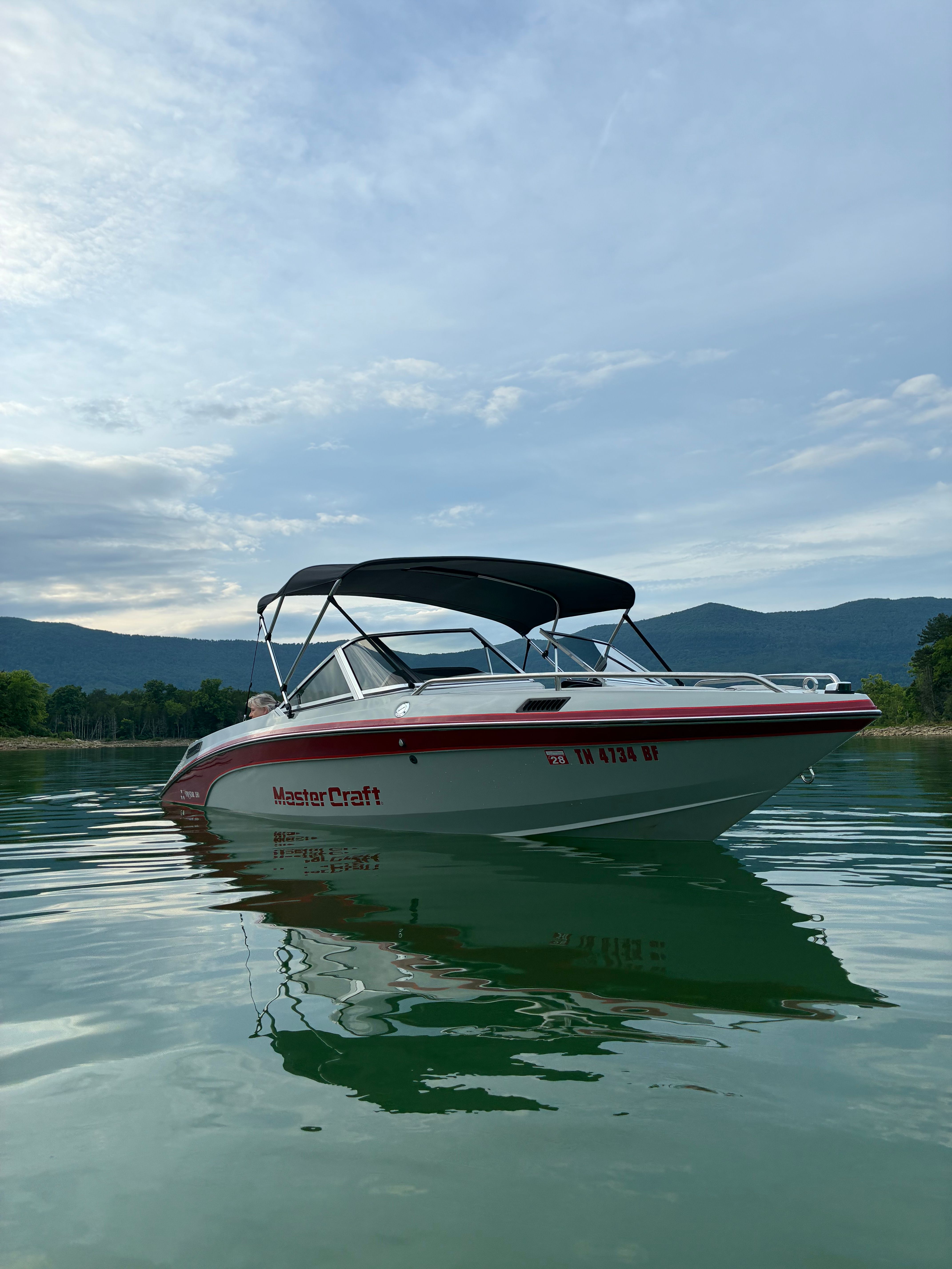 A 1989 MasterCraft TriStar 190 floats on calm water, surrounded by mountains.