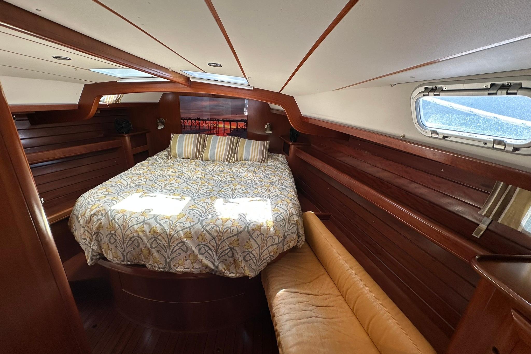 Luxurious cabin interior of a 2000 Beneteau 50 yacht with cozy bedding and wooden finishes.