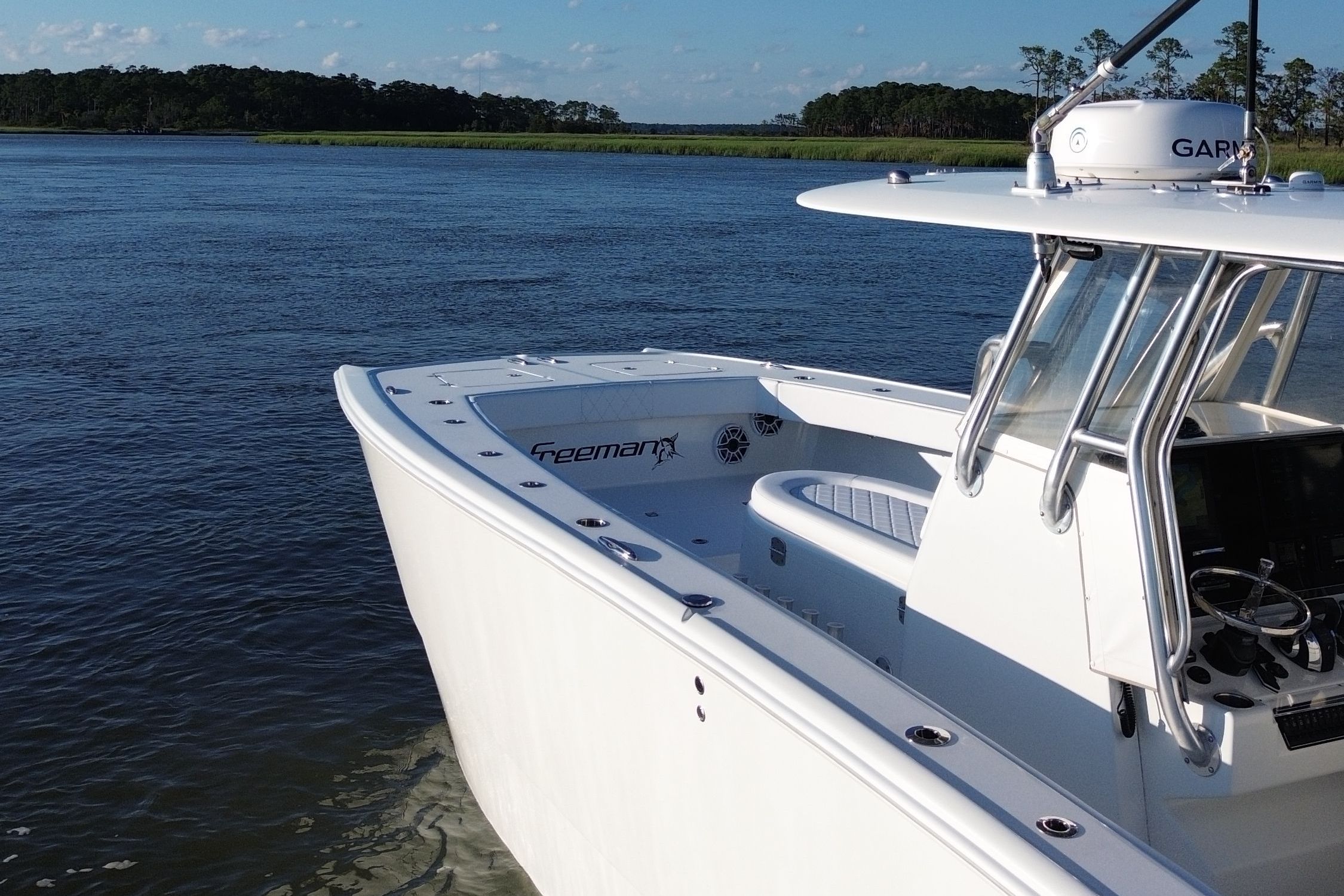 A white boat on calm water with a wooded shoreline in the background.