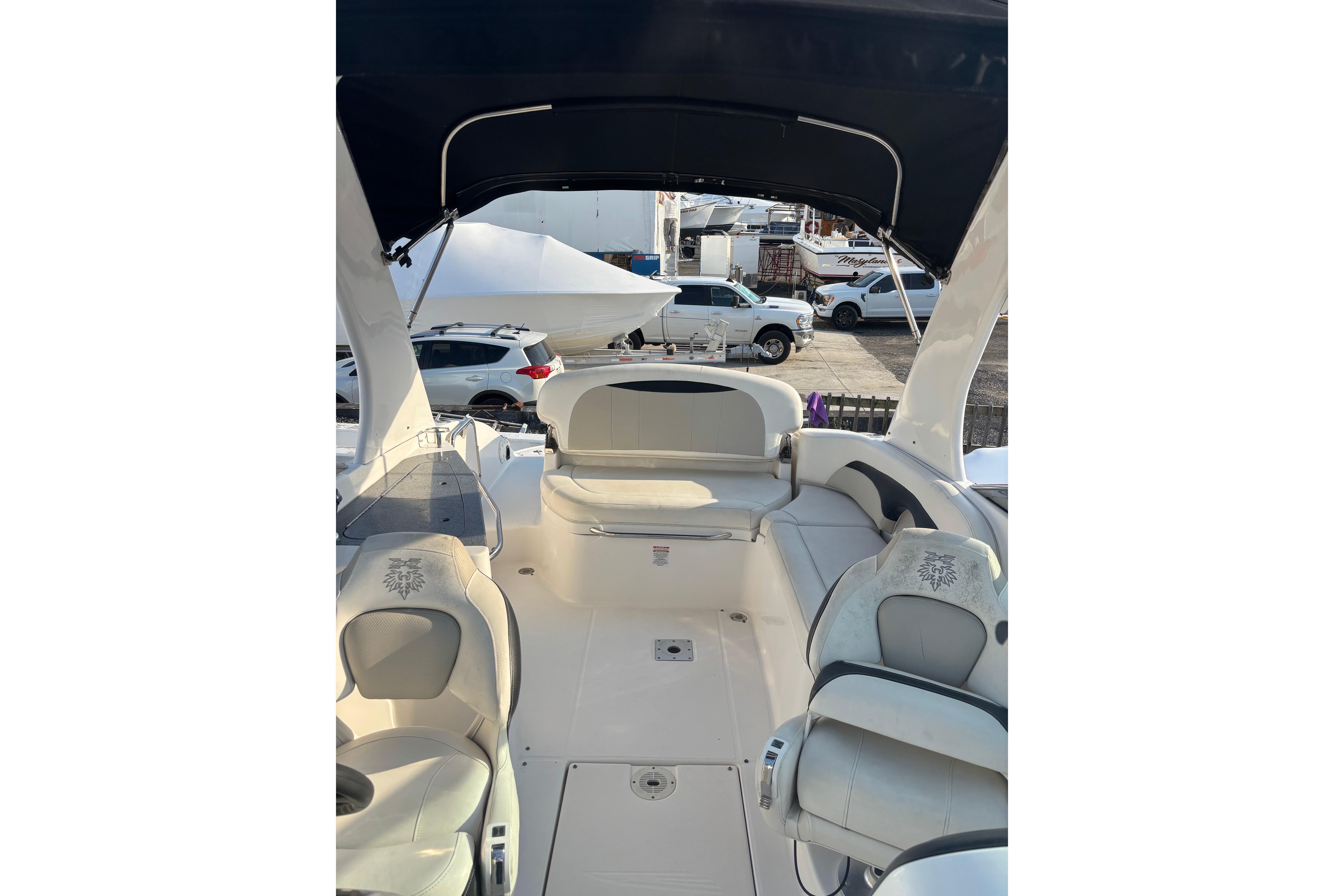 2012 Chaparral 267 SSX boat interior with seating and canopy, parked near vehicles.