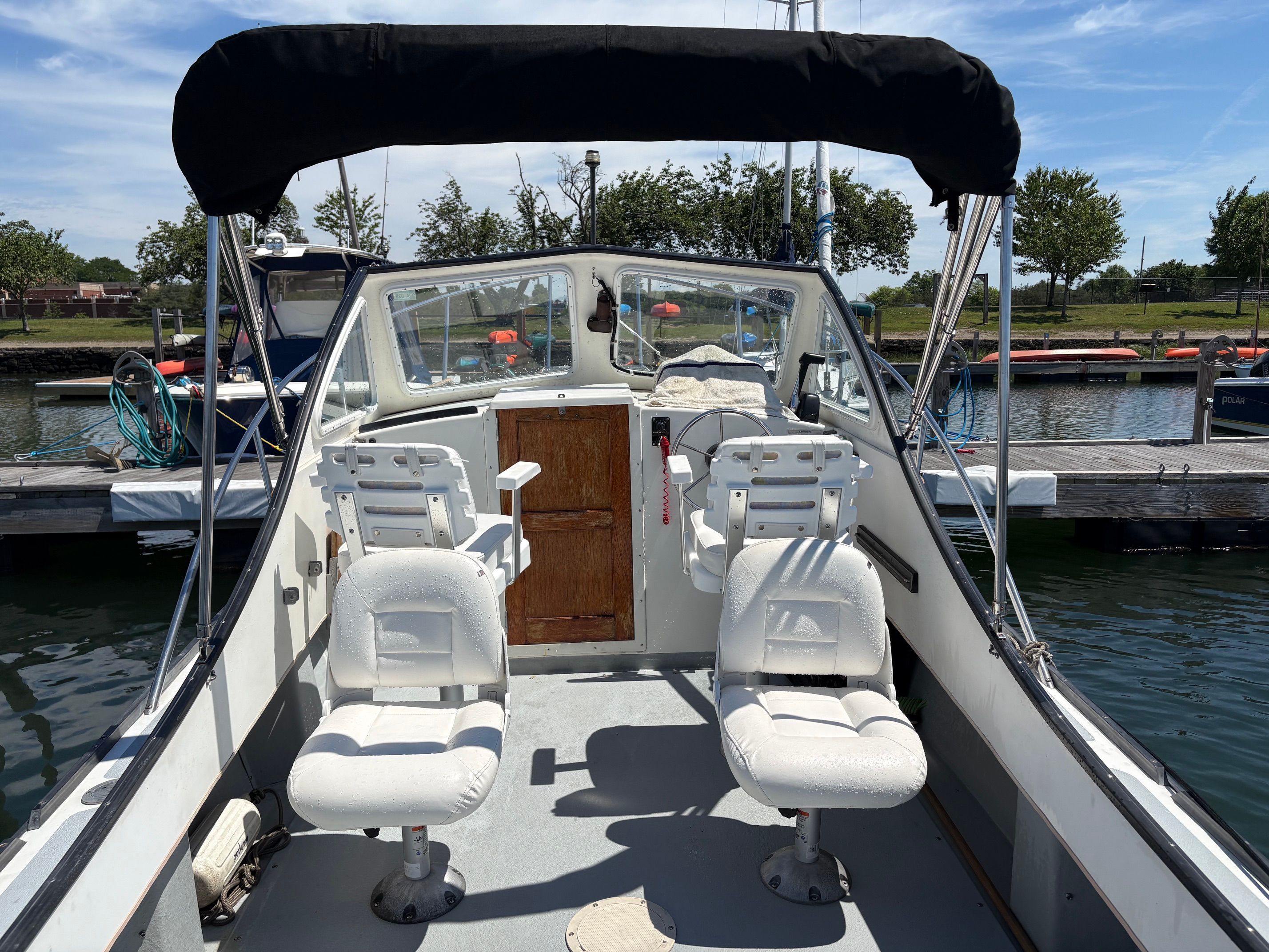 A 1990 Portsmouth 22 with two white seats and a black bimini top in a marina.