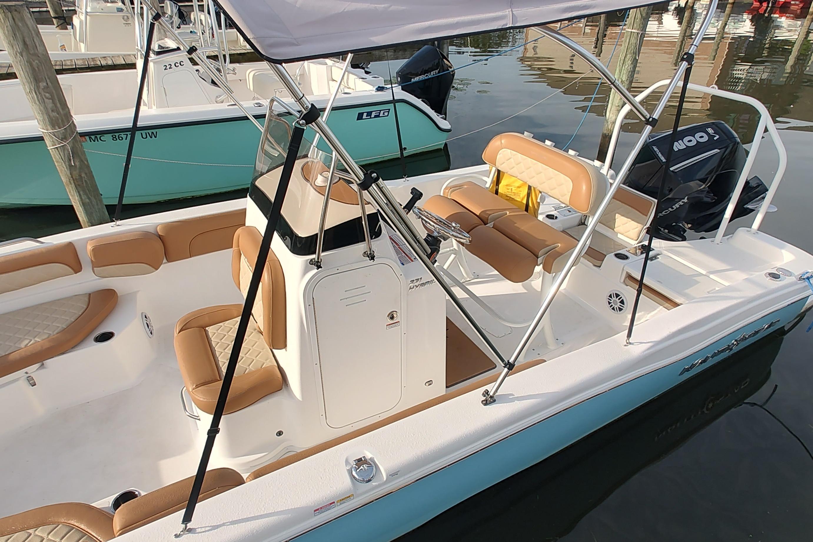 2026 NauticStar 231 Hybrid boat with tan seating and canopy docked in marina.