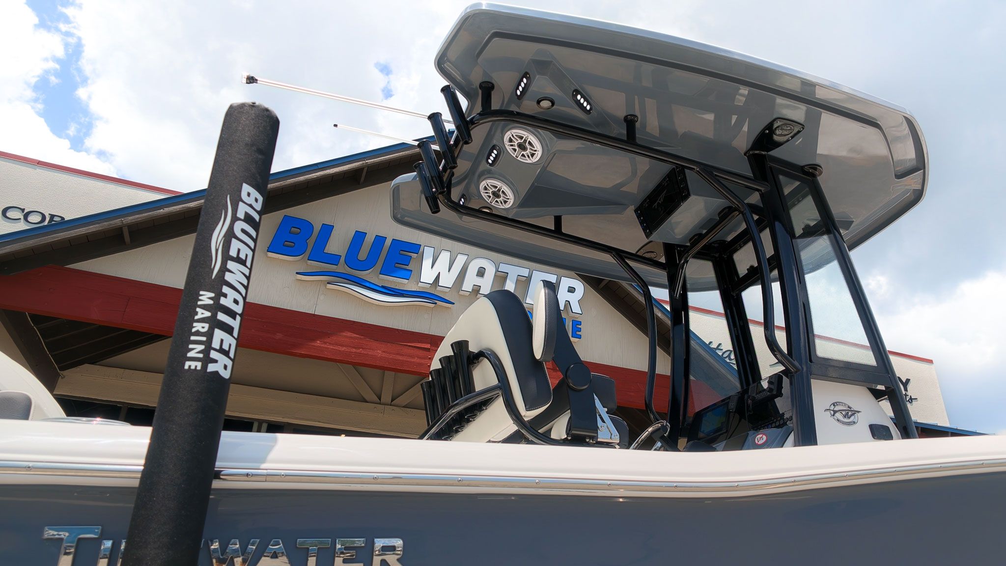 A modern boat with a T-top and speakers, in front of a building with "Bluewater Marine" signage.