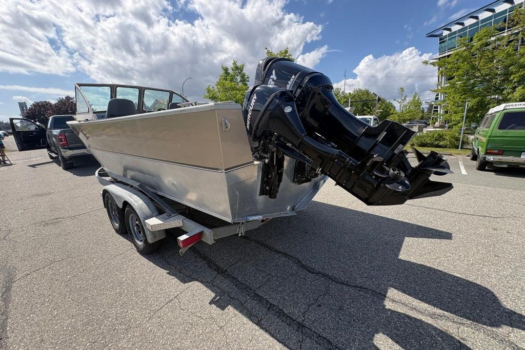 2009 Alumaweld Intruder Outboard 22 boat on trailer, parked outdoors under a cloudy sky.