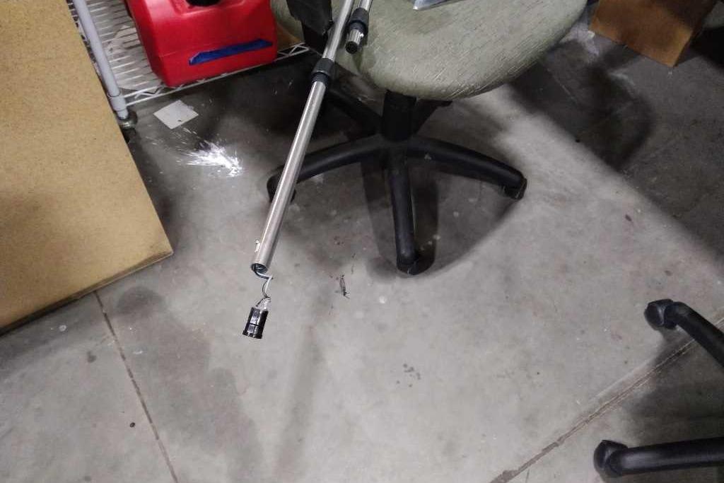 Office chair on concrete floor with a metal rod and hook nearby.