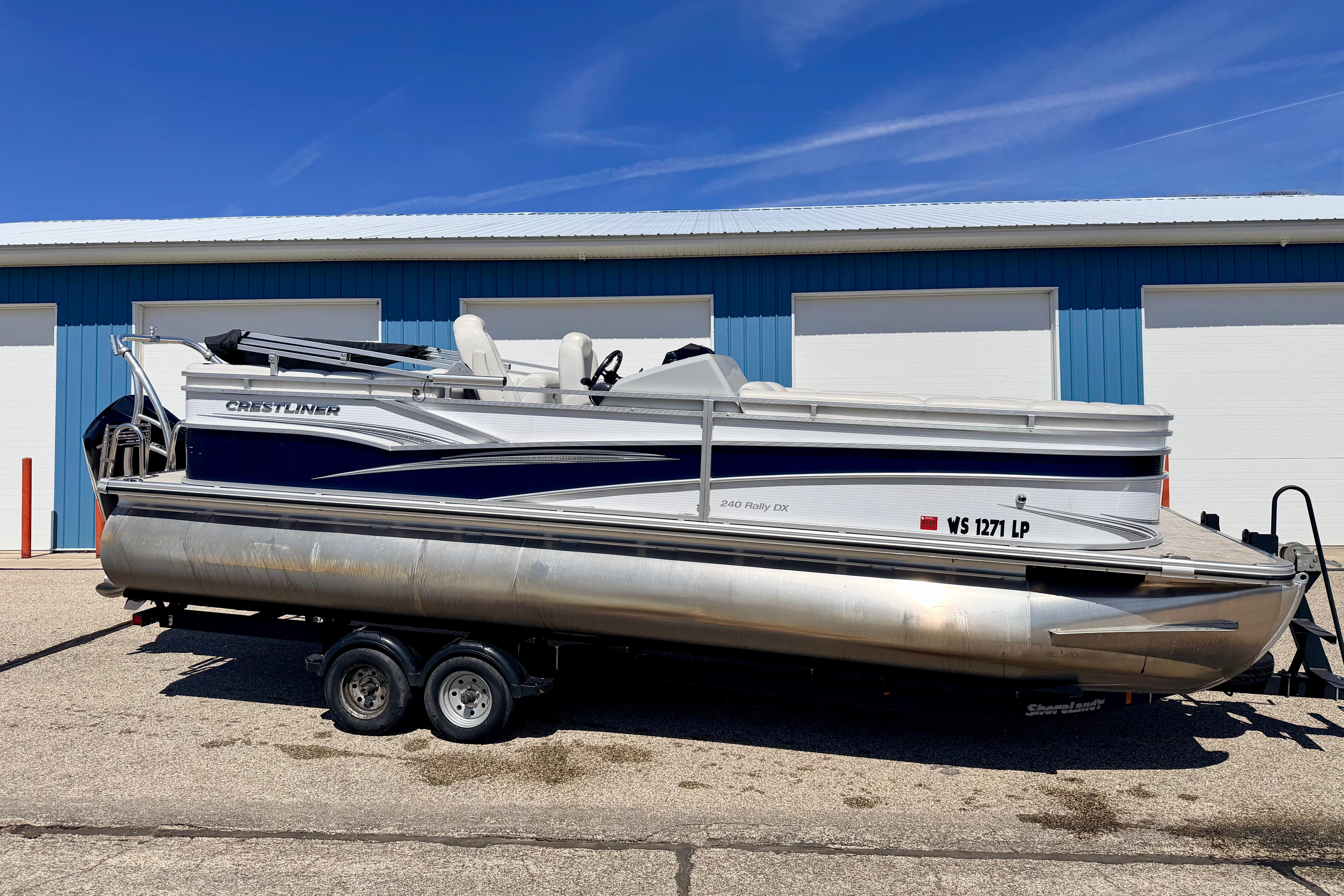 2019 Crestliner 240 Rally DX CW pontoon boat on trailer, parked outside a blue building.