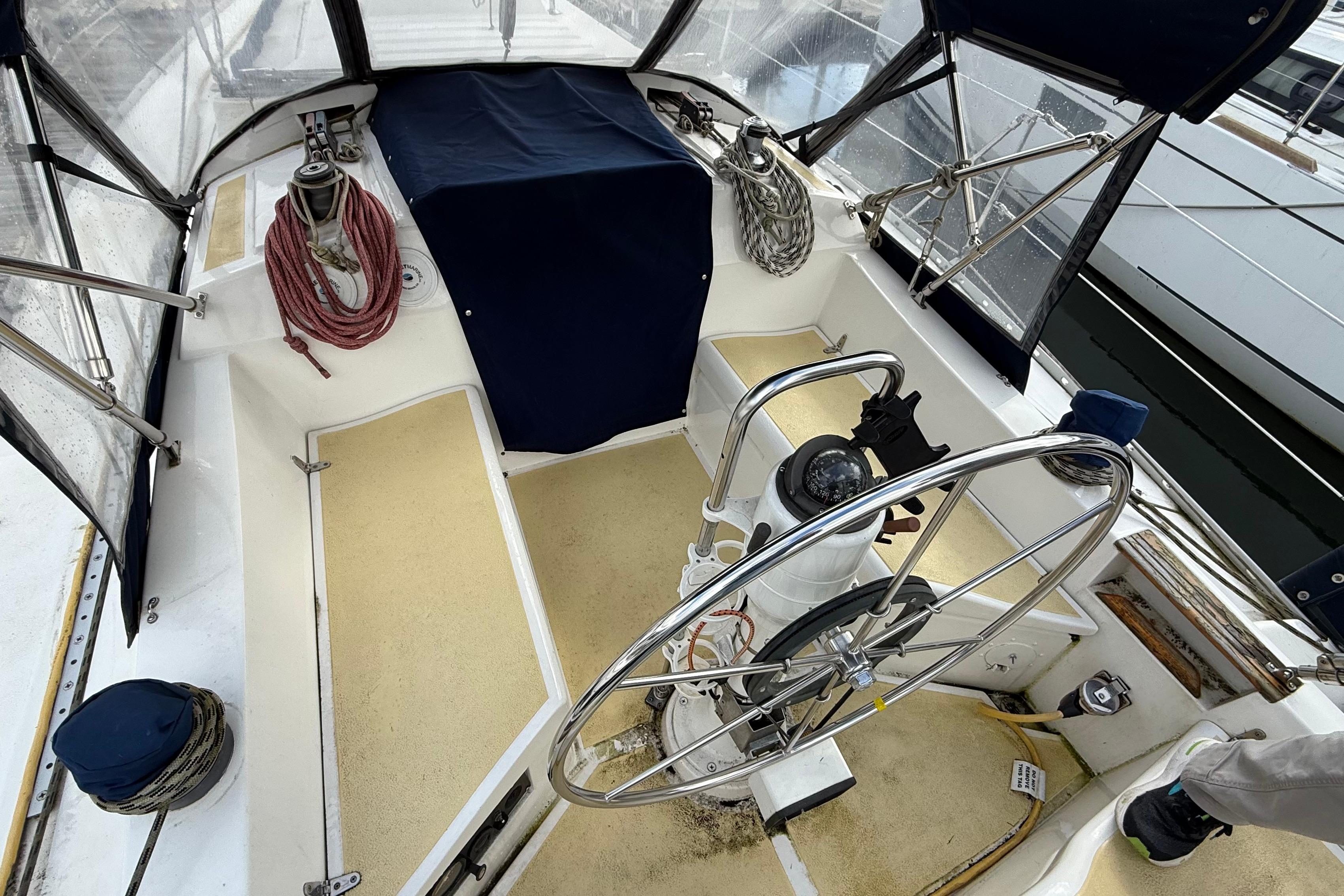 1984 Hunter 31 sailboat cockpit with steering wheel and ropes, covered seating area.