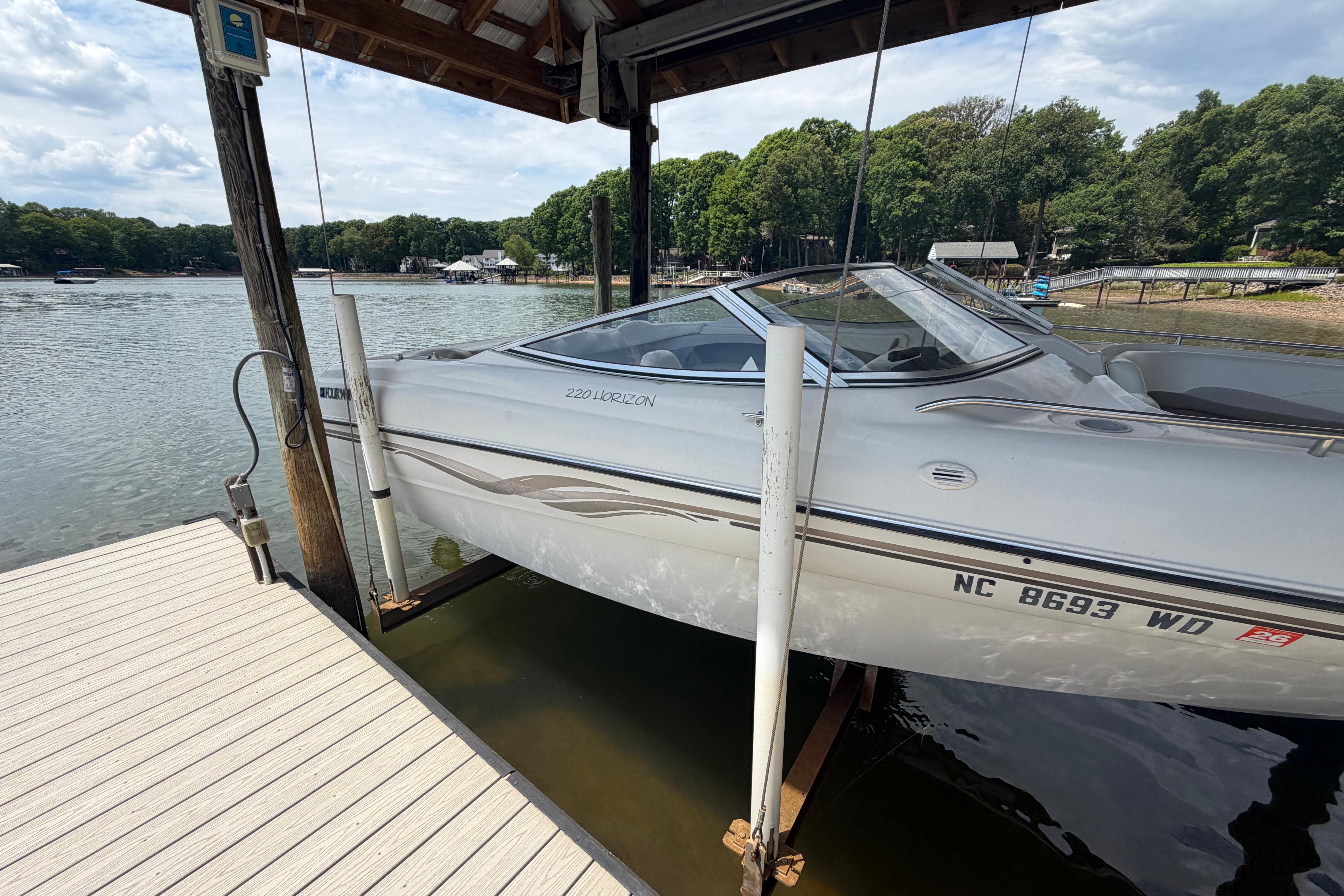 1998 Four Winns 220 Horizon boat docked on a lake under a wooden shelter.