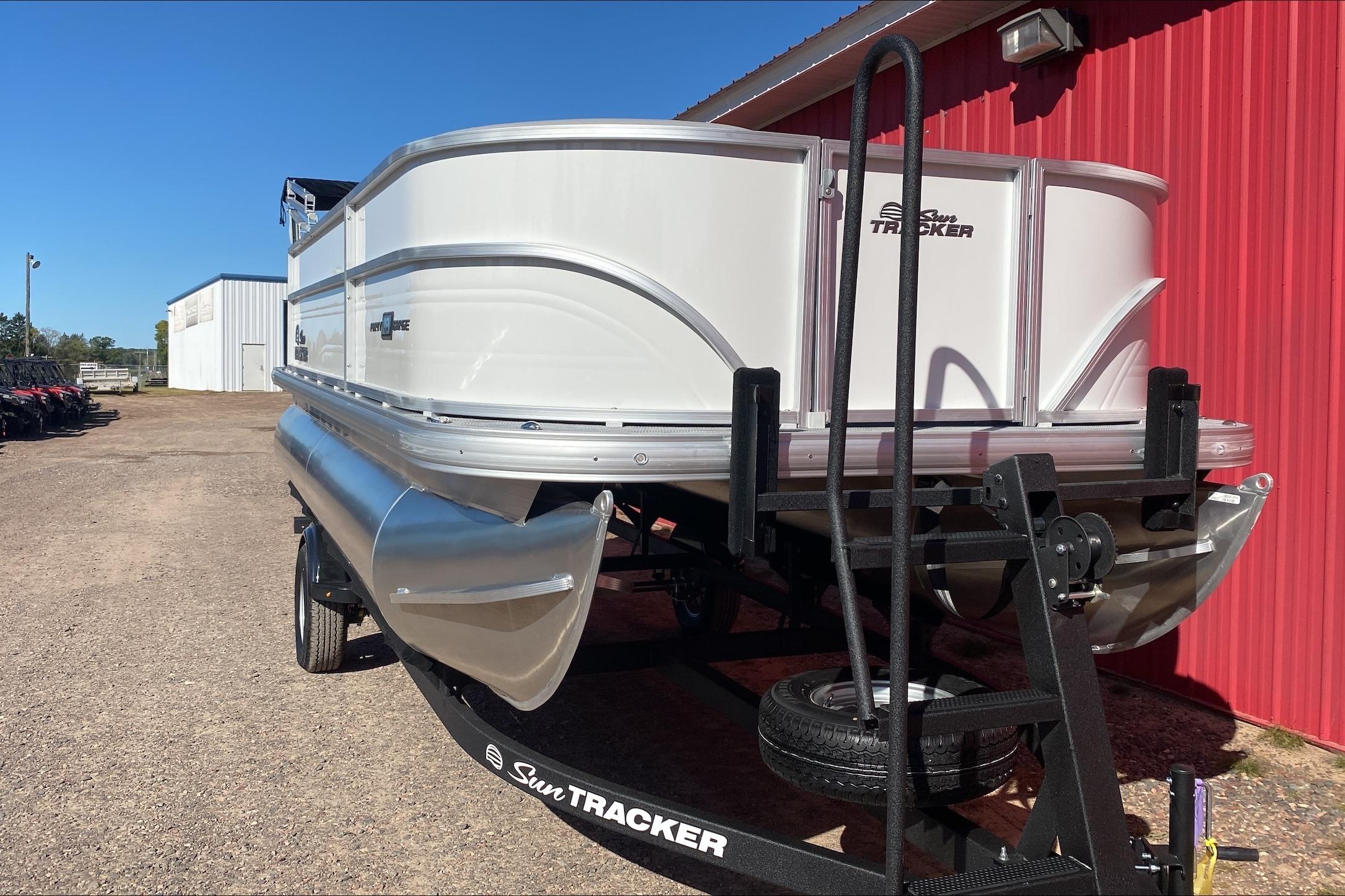 2026 Sun Tracker Party Barge 18 DLX pontoon boat on trailer near red building.