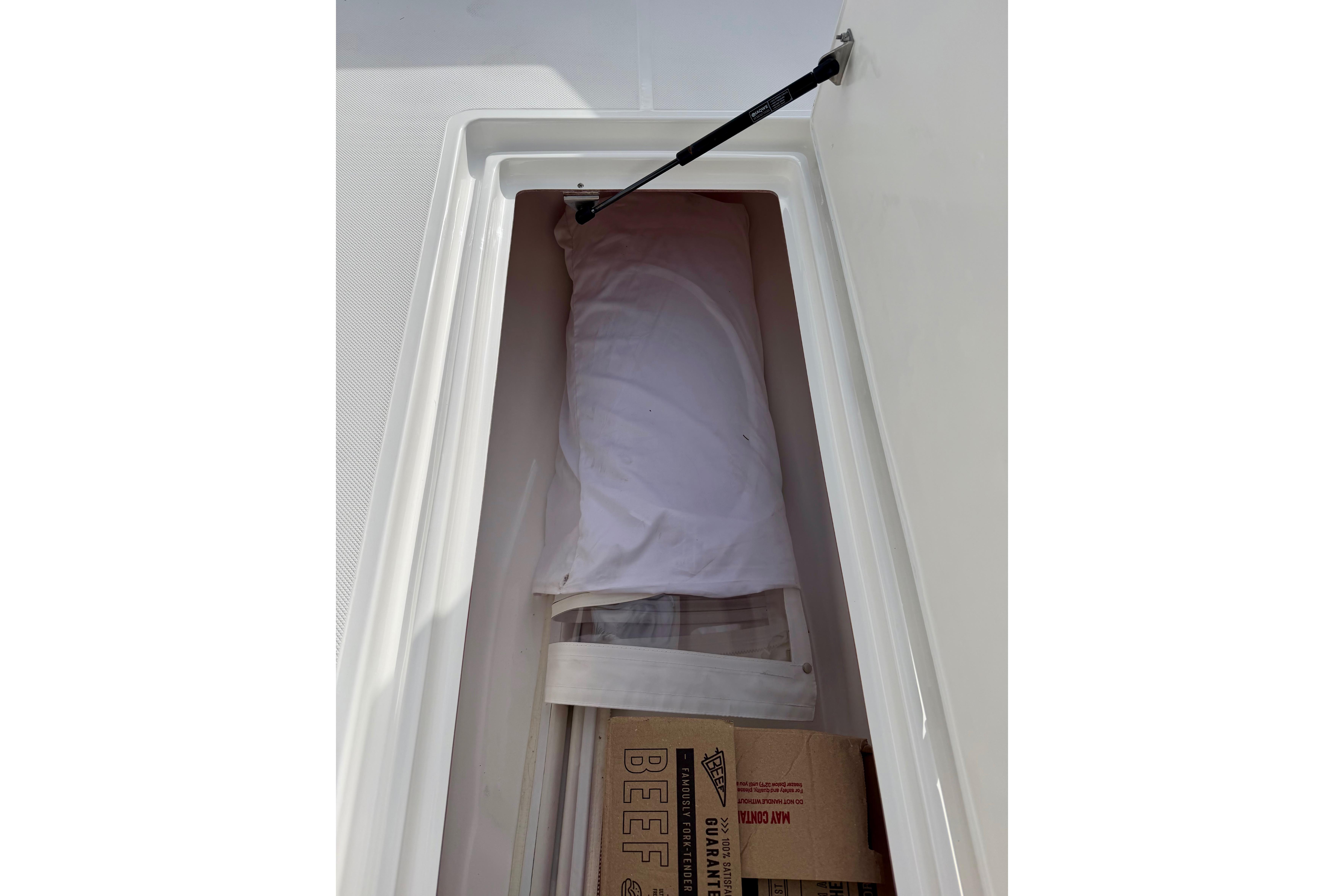 Storage compartment in 2025 Ocean Master 296 Center Console boat, containing wrapped items and boxes.