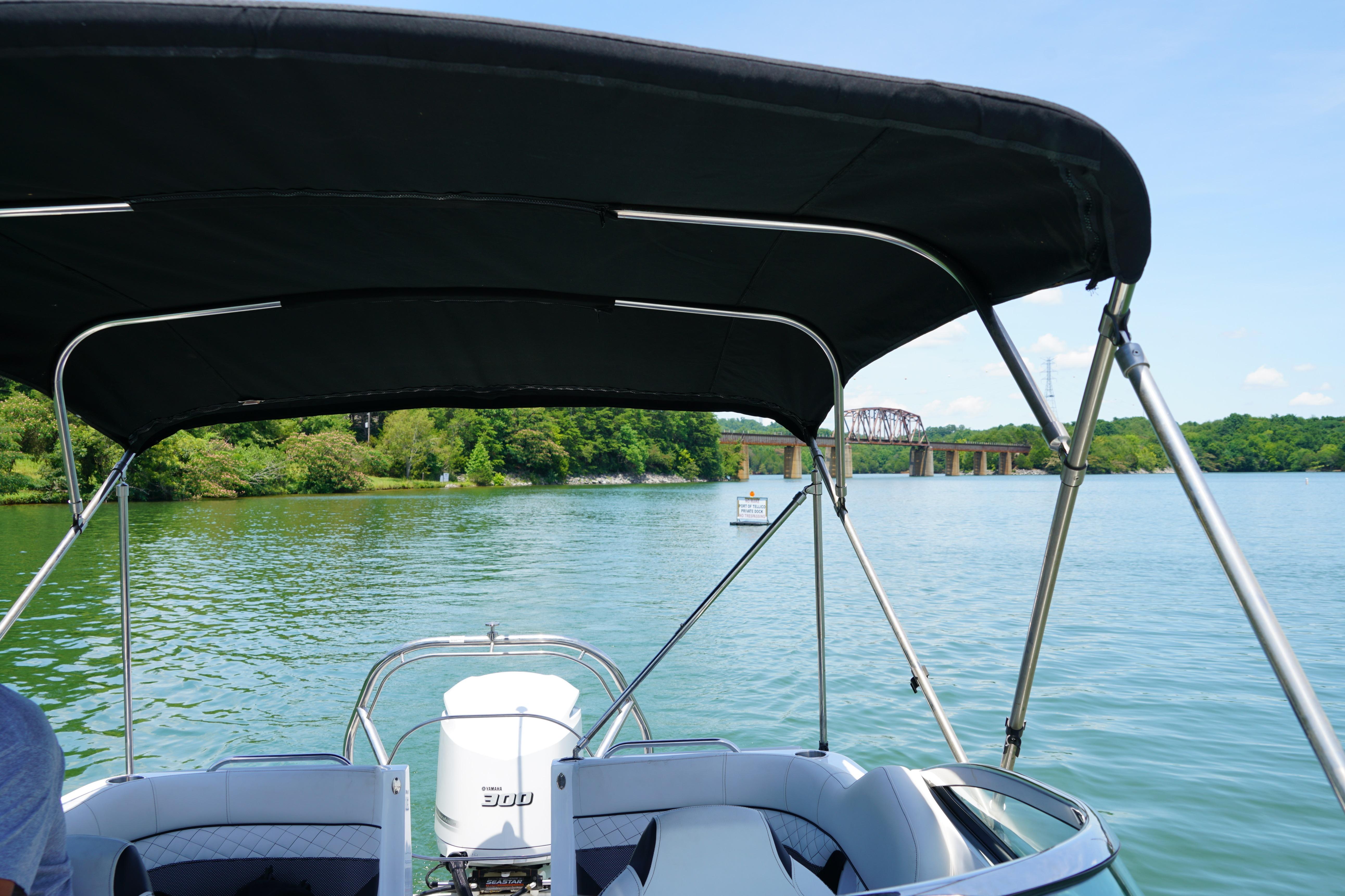 2020 Hurricane SunDeck 2486 OB boat cruising on a scenic lake with bridge view.