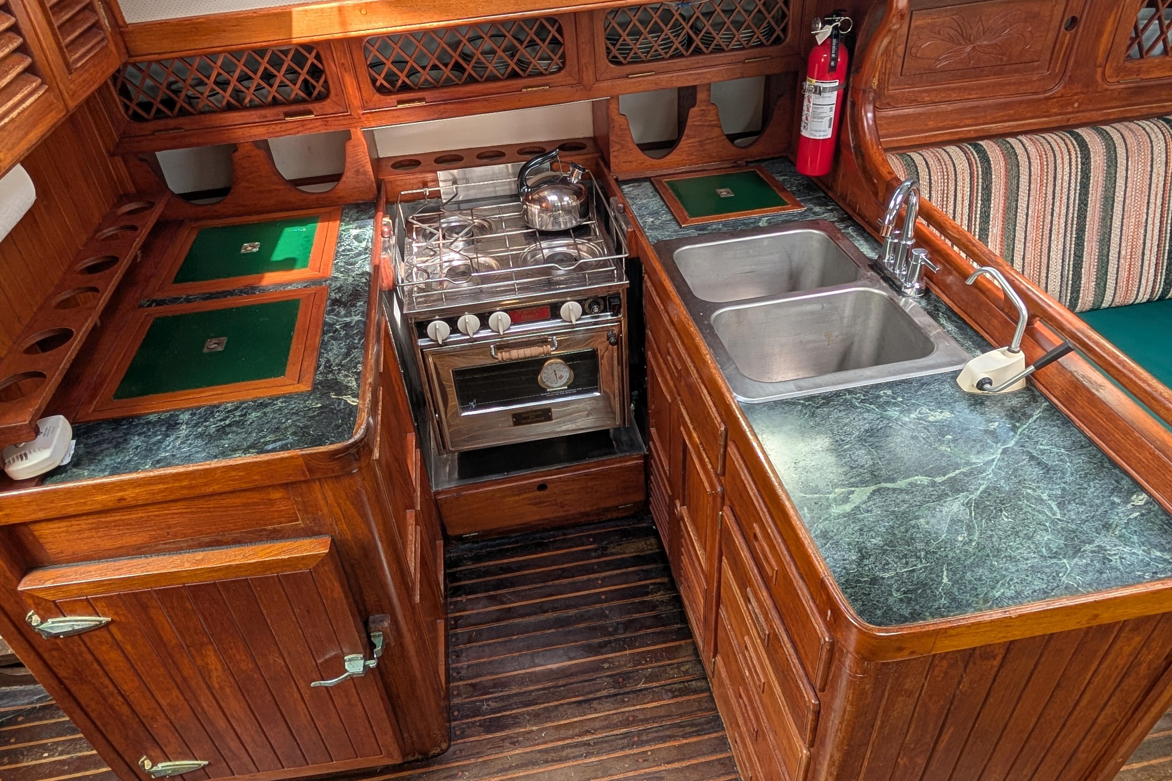 1983 Perry 41 yacht kitchen with wood cabinetry, dual sinks, and a stainless steel stove.