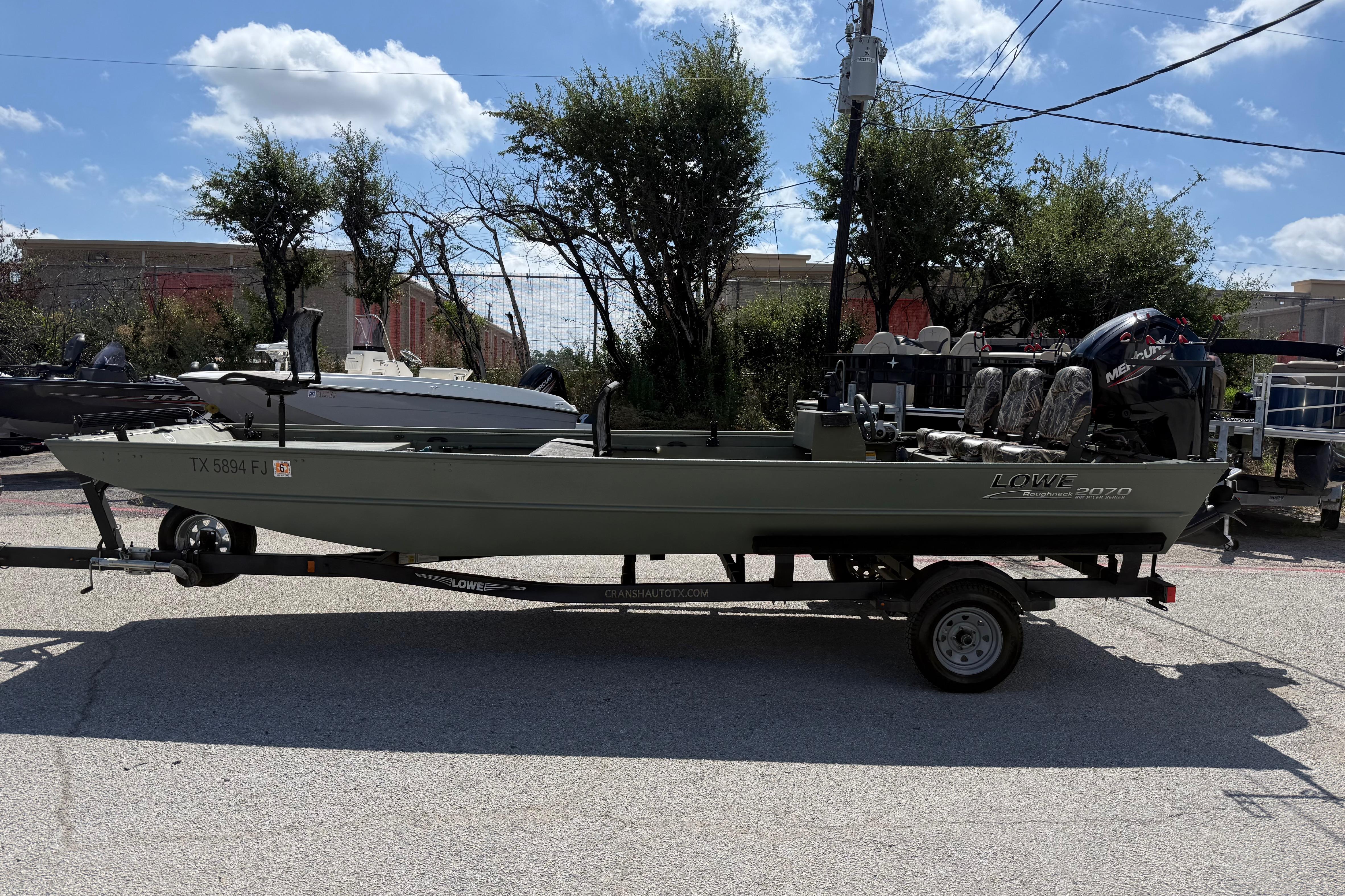 A 2020 Lowe Roughneck 2070 Big River boat on a trailer, surrounded by trees.