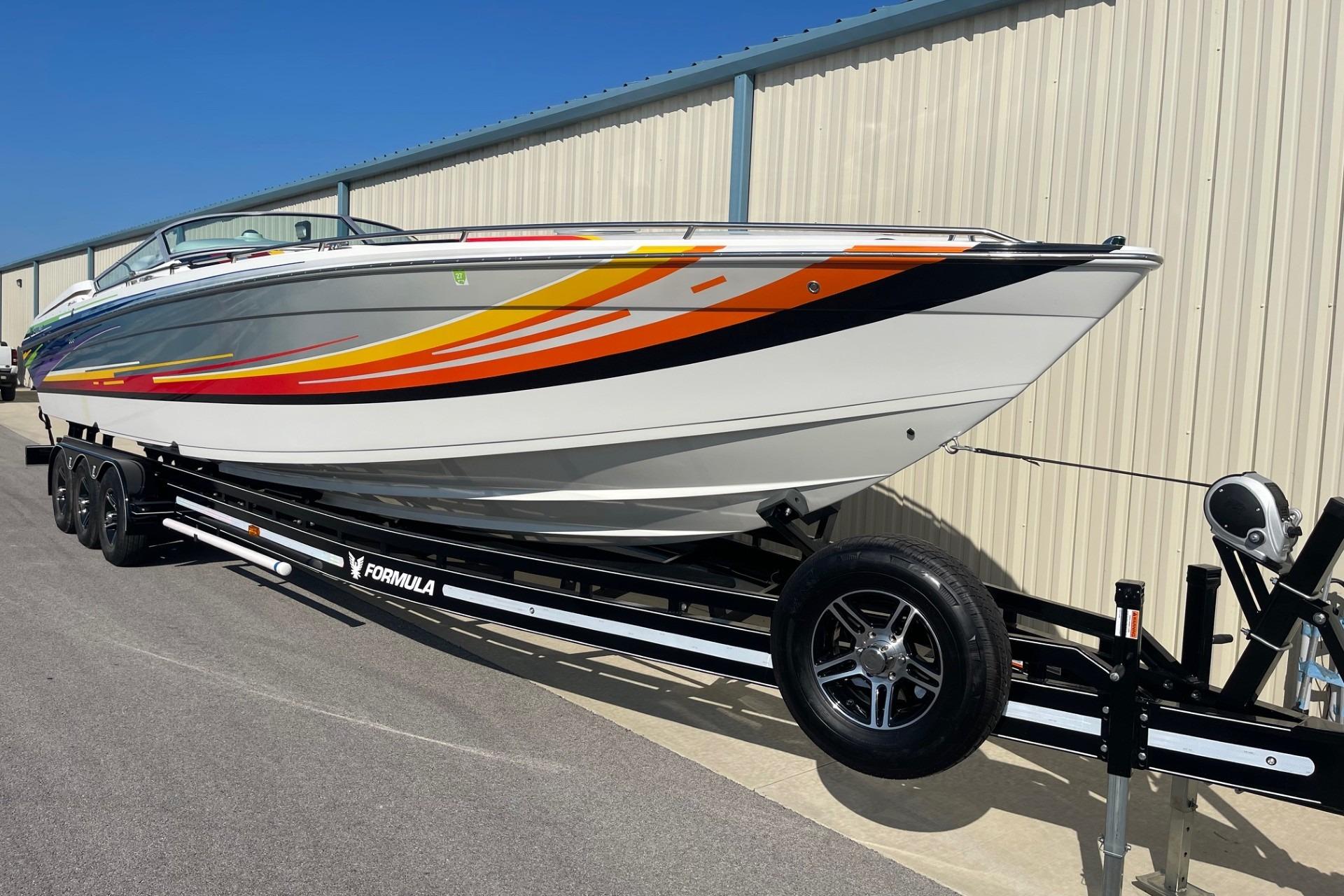 2004 Formula 382 FASTech boat on trailer, vibrant stripes, parked by a metal building.