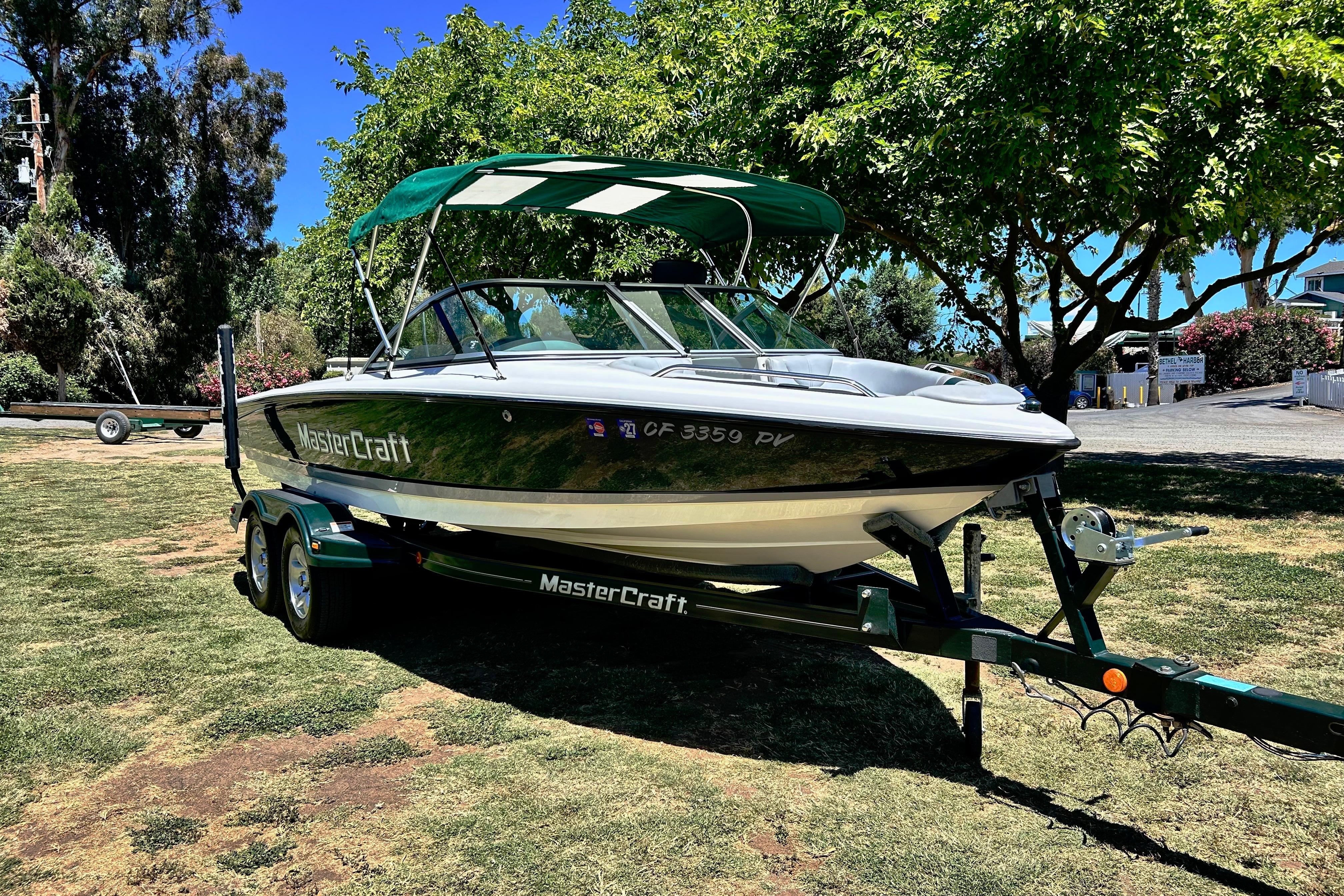 2002 MasterCraft ProStar 197 boat on trailer, parked on grass under trees.