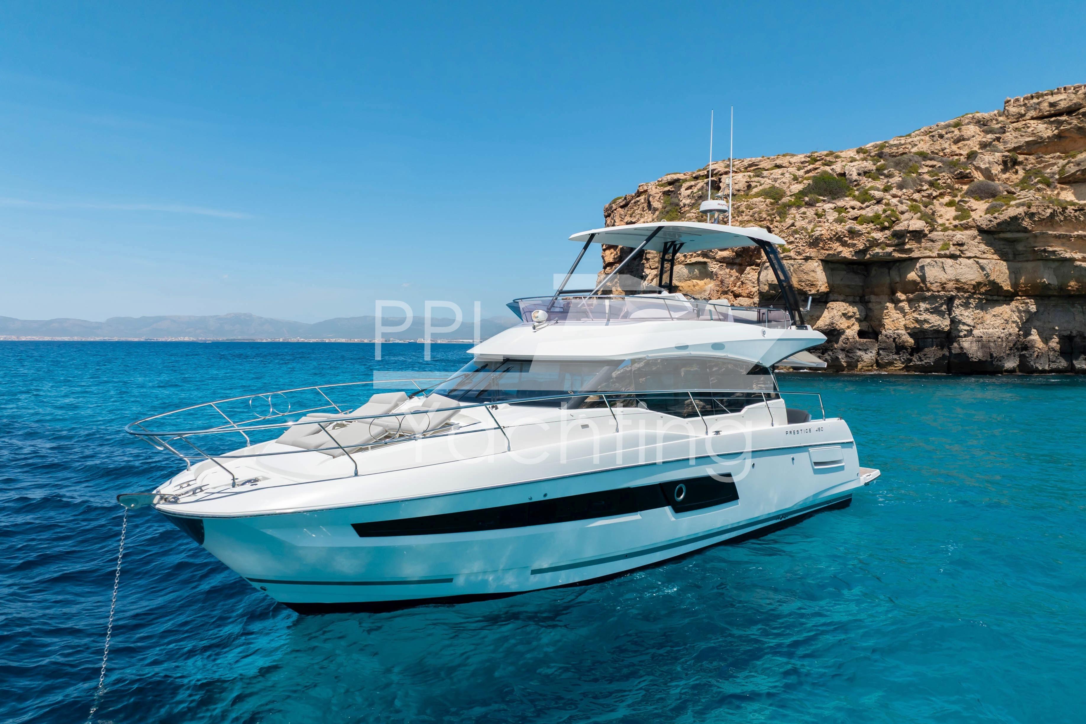 Luxurious 2019 Prestige 460 yacht anchored in clear blue waters near rocky coastline.