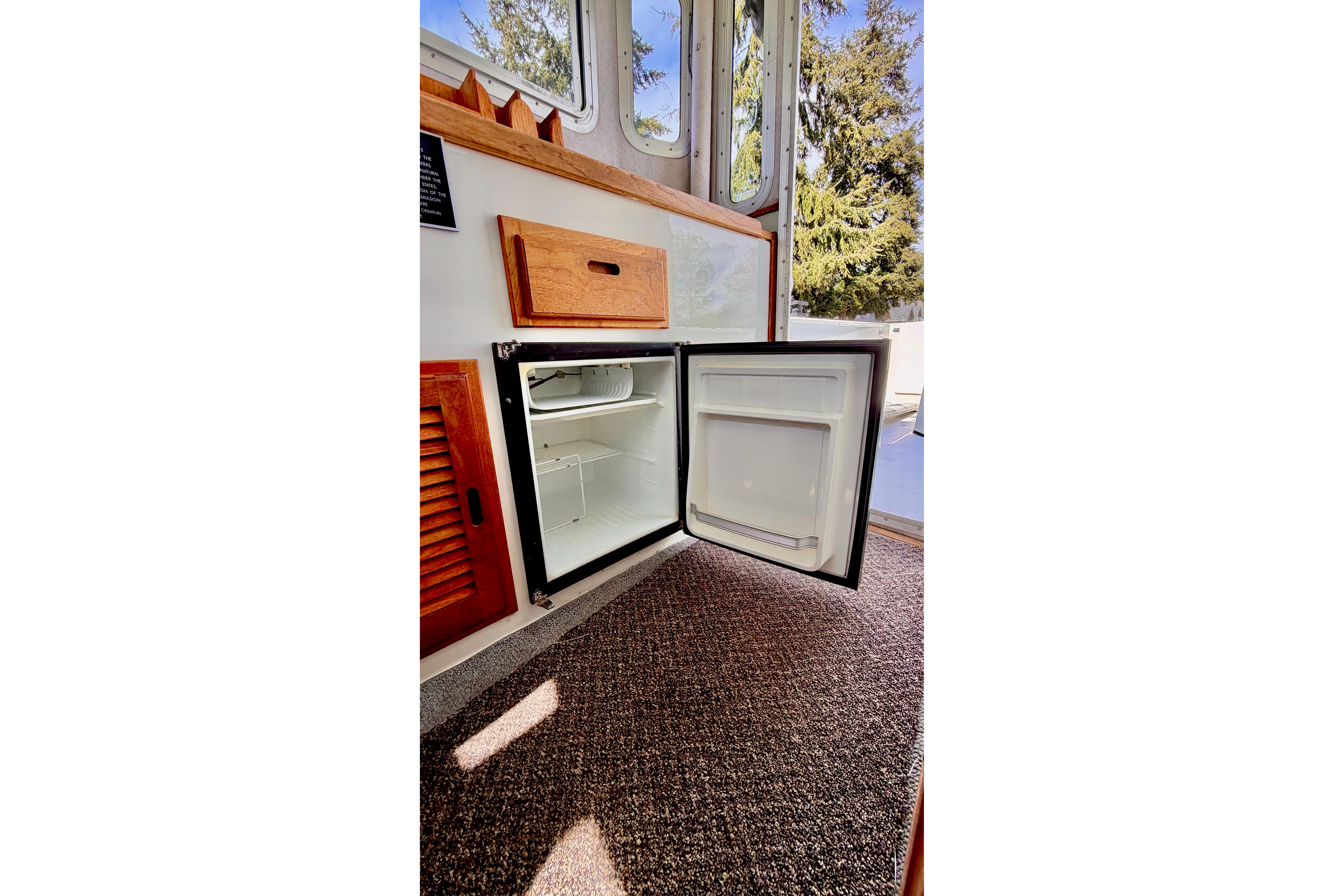 Open mini fridge inside 2006 Osprey Legend boat, with wooden cabinetry and carpeted floor.