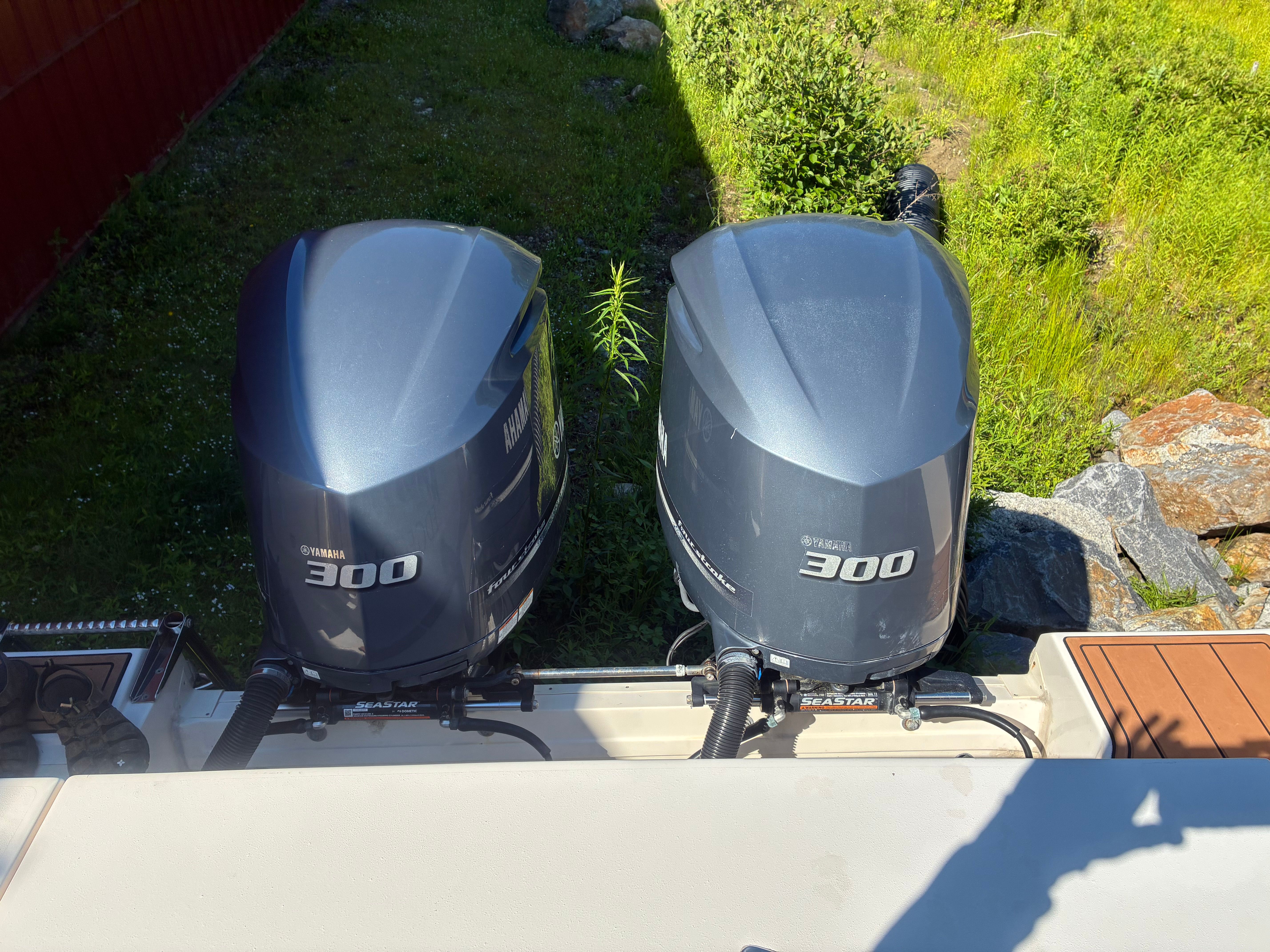 Two outboard engines on a boat, surrounded by green grass and rocks.