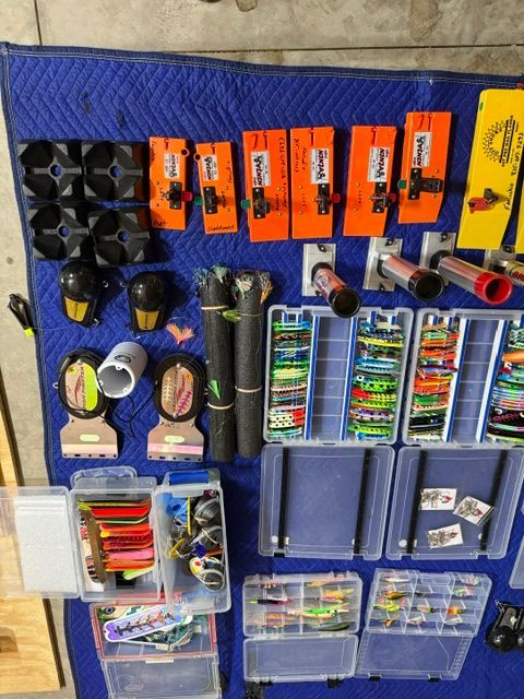 Various fishing gear is spread out on a blue blanket, including lures and fishing reels.