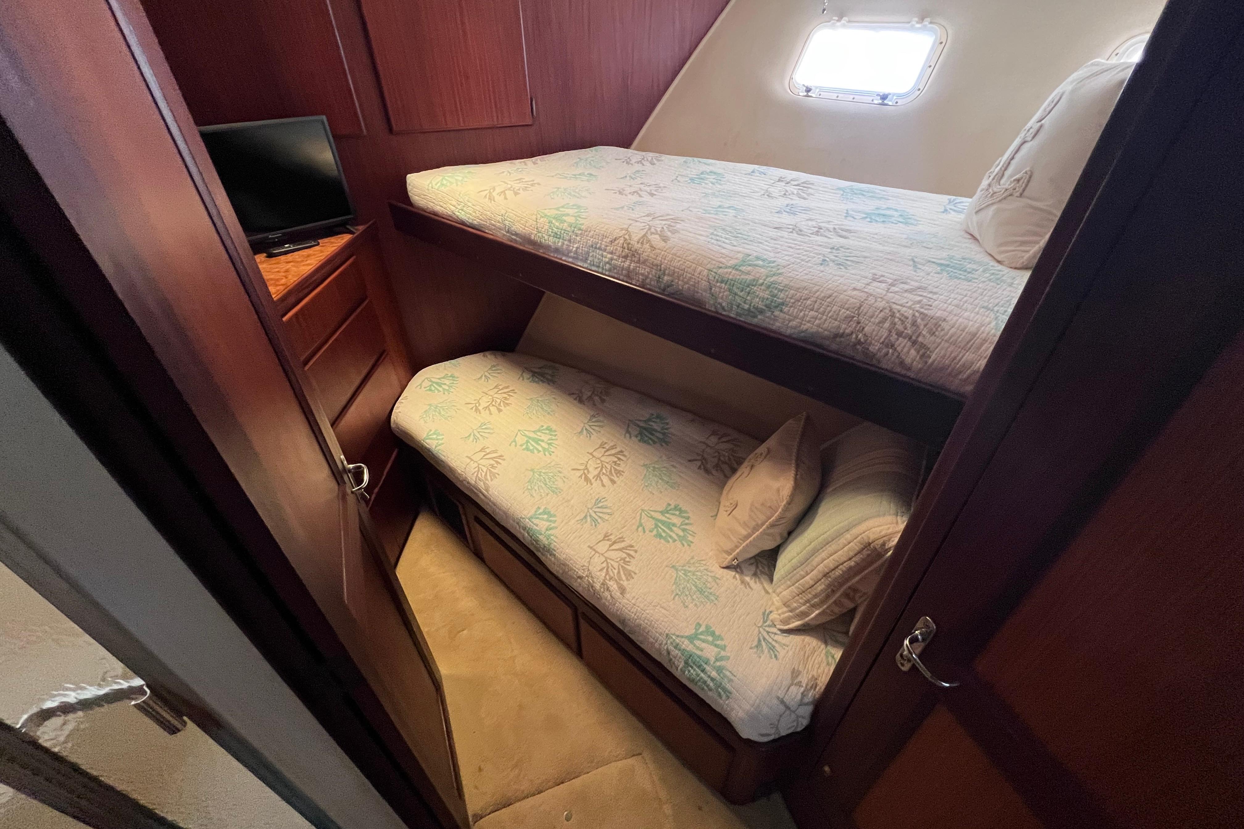 Cozy bunk beds in 1987 Hatteras 70 Cockpit Motor Yacht cabin with small window and TV.