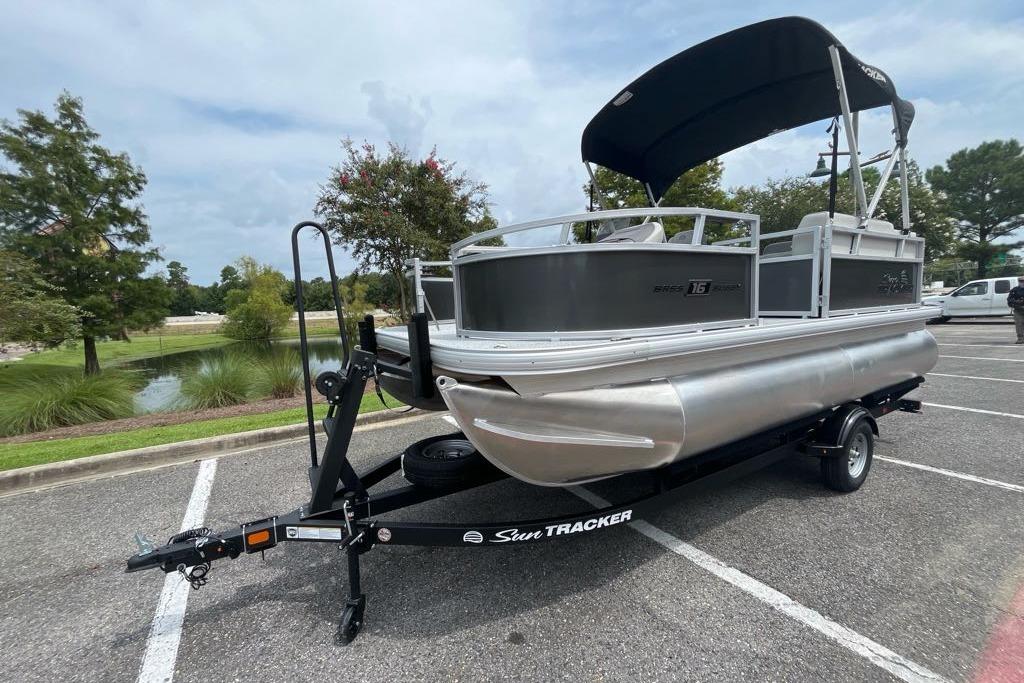 2026 Sun Tracker Bass Buggy 16 XL Select pontoon boat on trailer in parking lot.