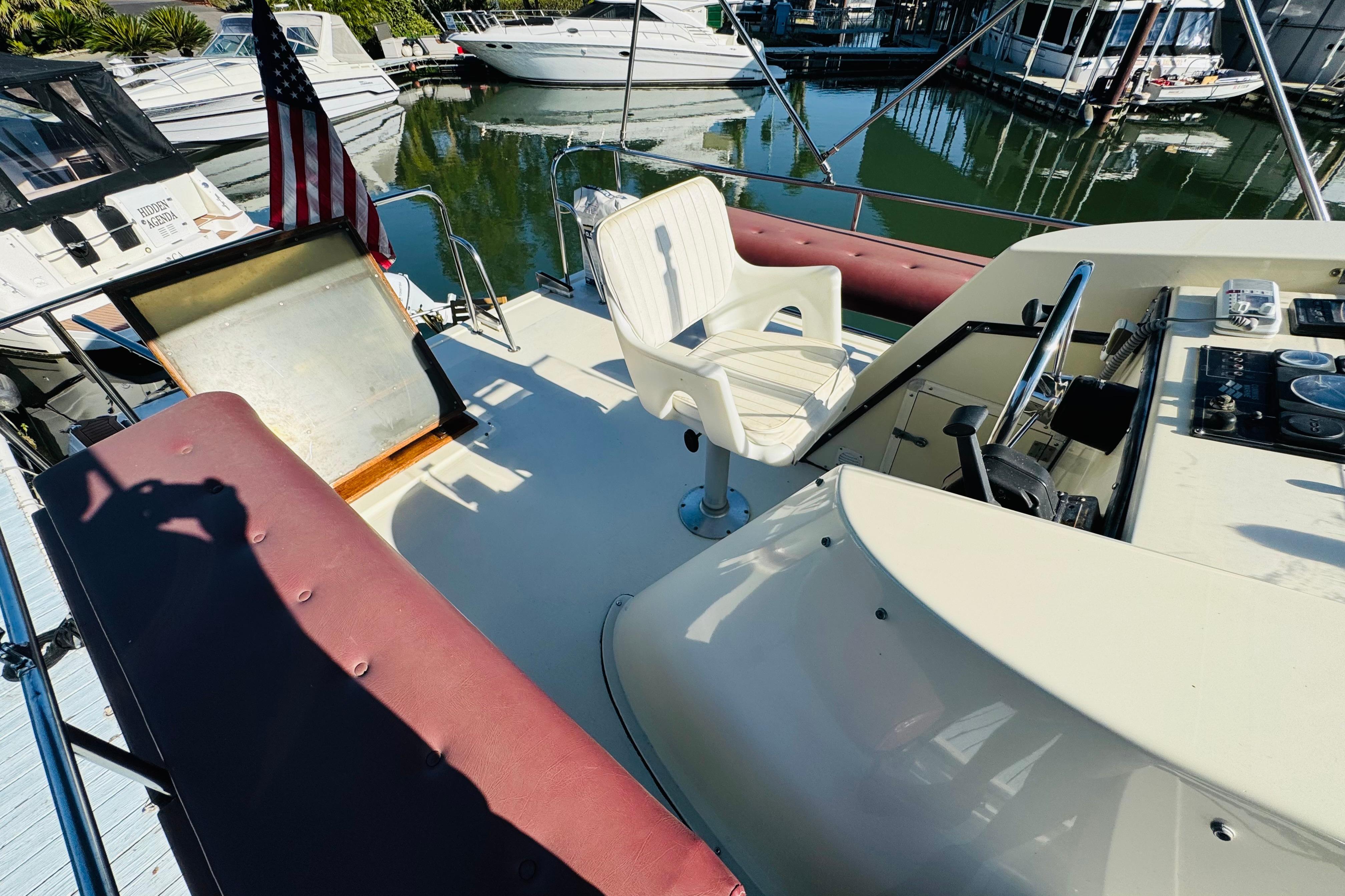 1996 Nordic Tug 32 boat deck with seating, steering wheel, and American flag in marina.