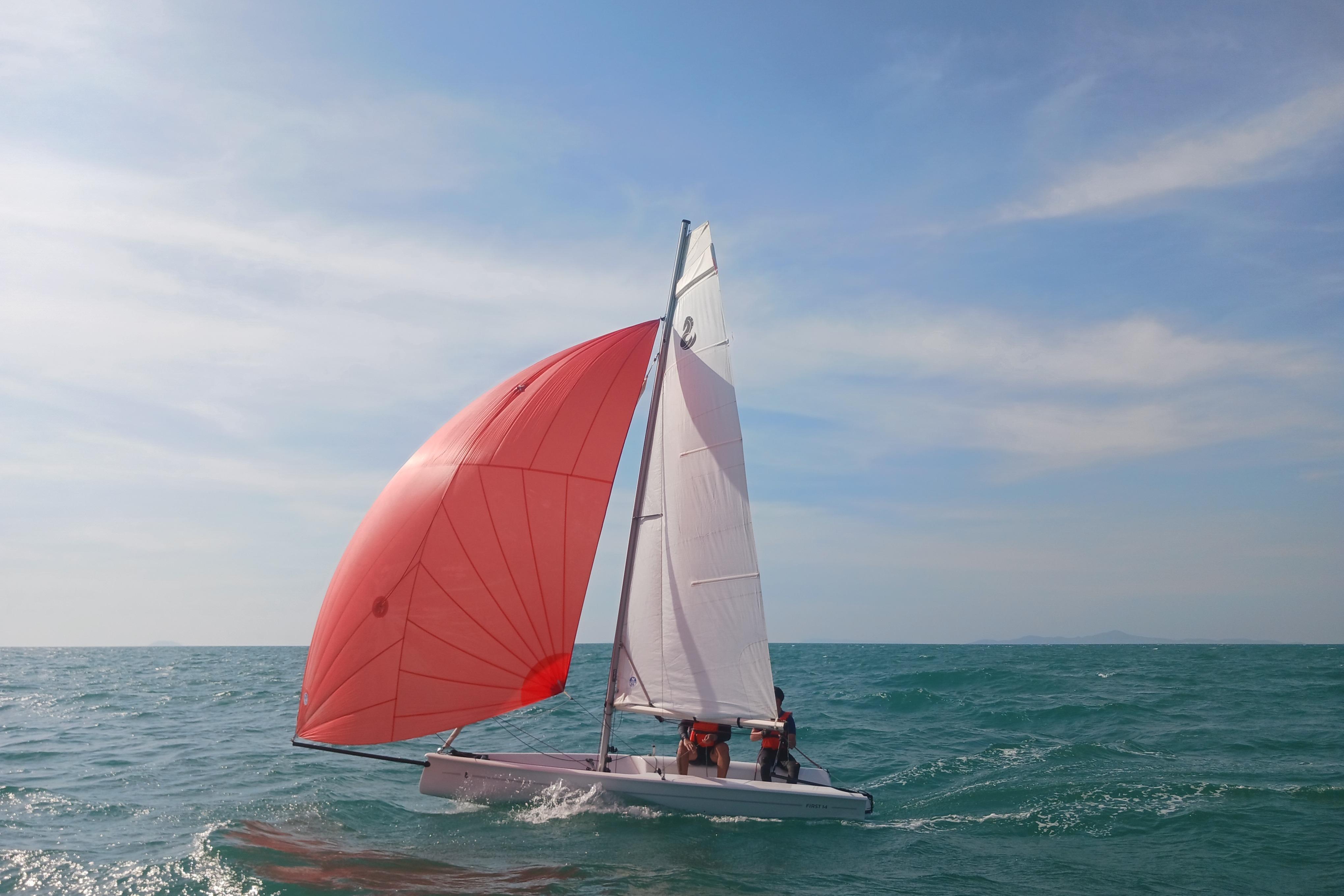 Sailing Beneteau First 14, 2021 model, with red spinnaker on open sea.
