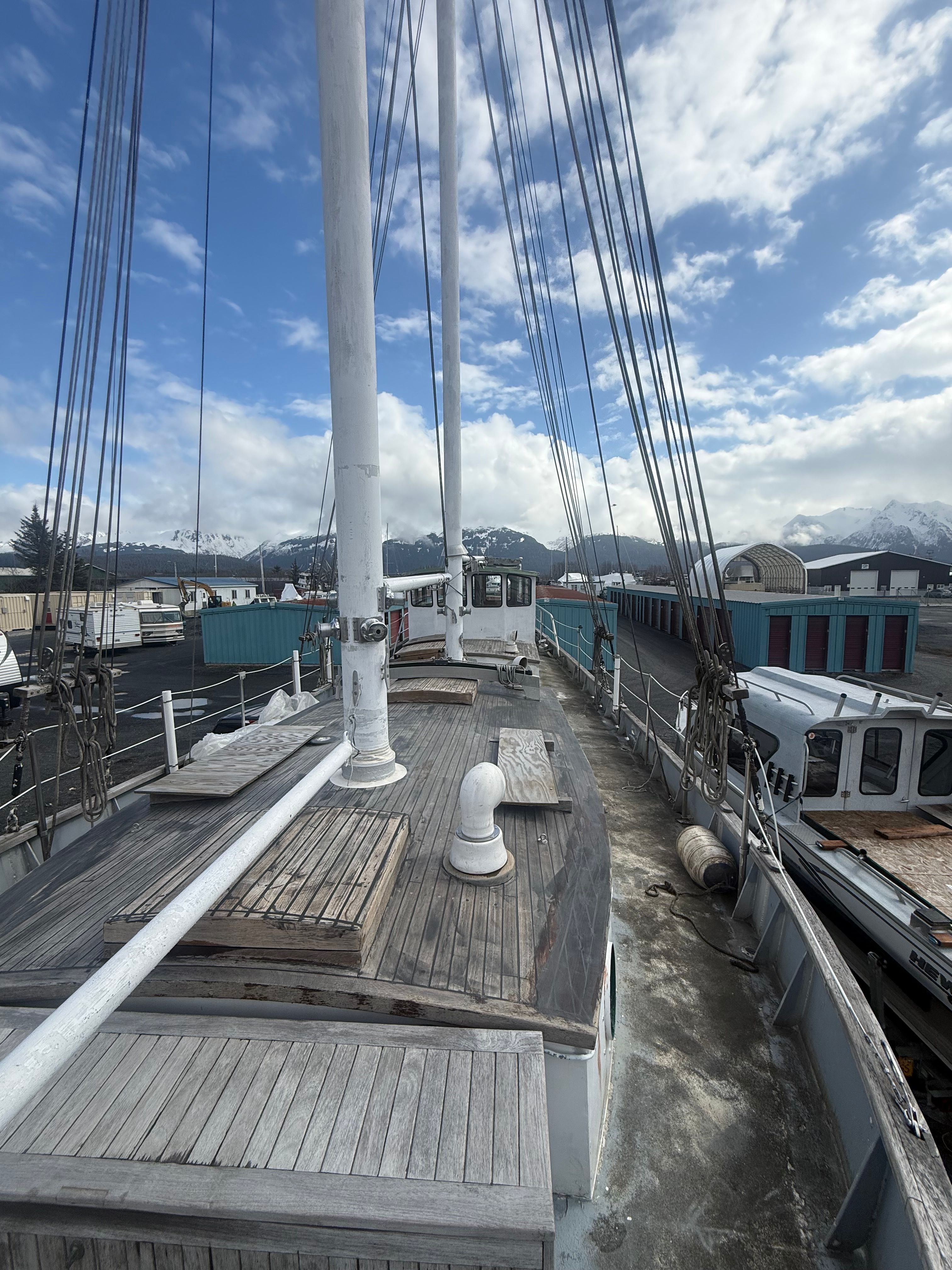 A wooden deck of a schooner sailboat with two masts, surrounded by a harbor and mountains.