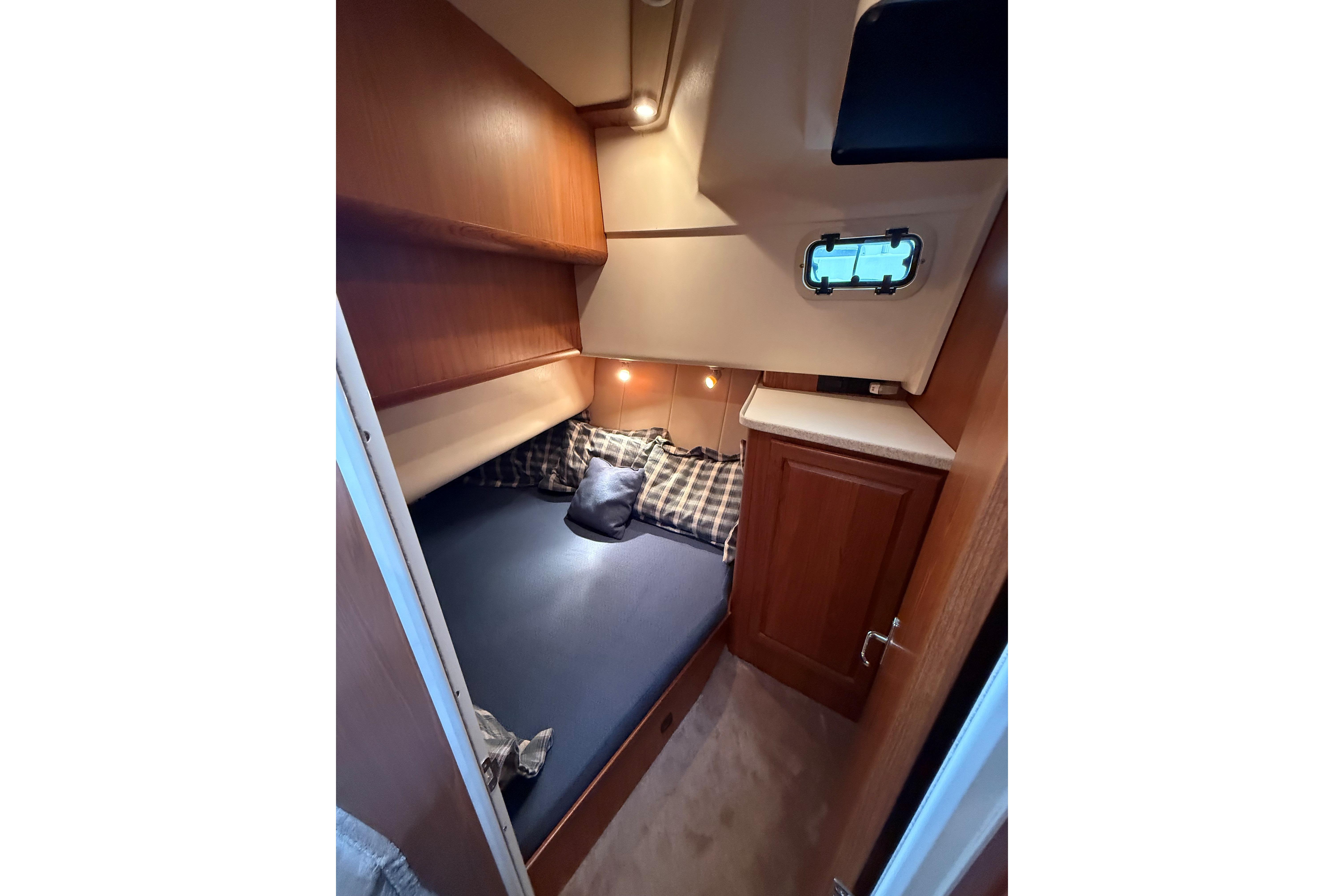 Cozy cabin interior of 1999 Mainship 350 Trawler with bed and wooden cabinetry.
