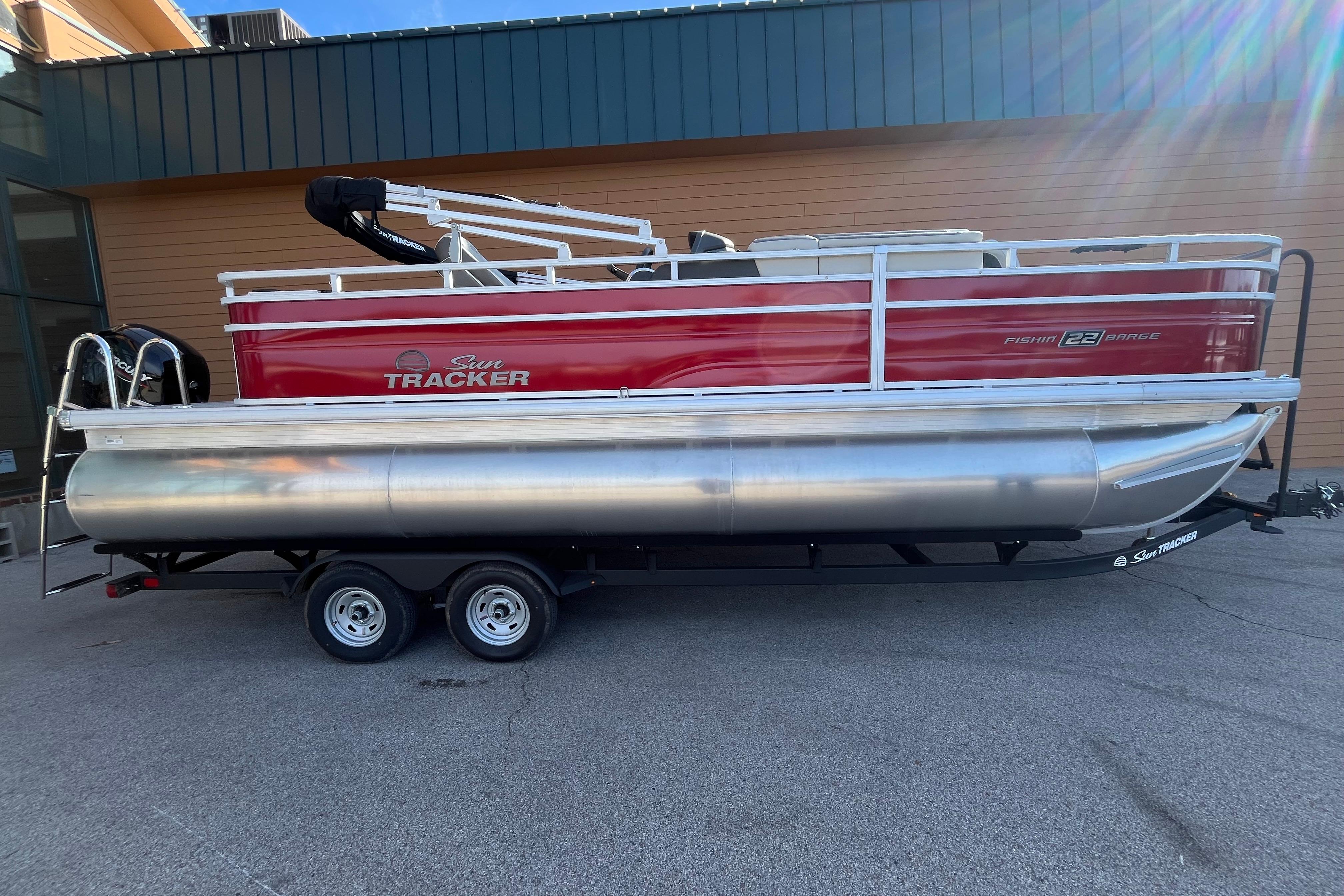 2026 Sun Tracker Fishin' Barge 22 XP3 pontoon boat on trailer, red and silver design.