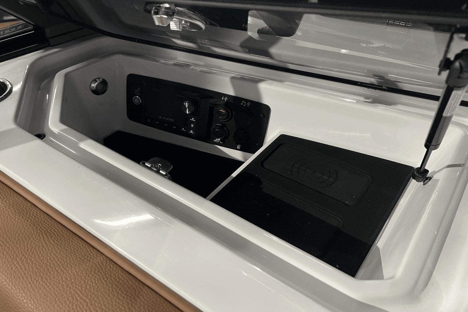 2023 Nautique Super Air Nautique S25 storage compartment with audio controls and wireless charging pad.
