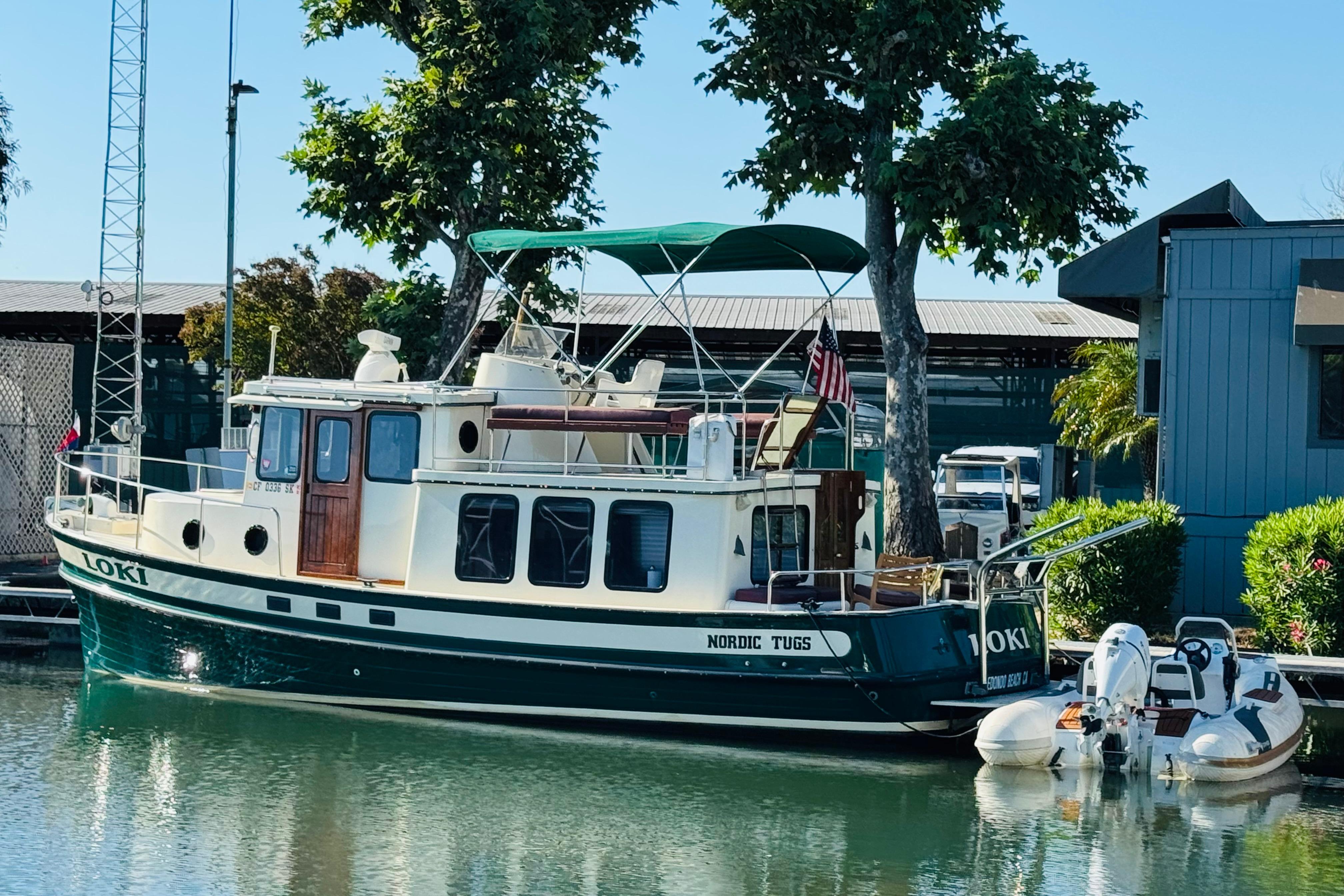 Nordic Tug 32 boat from 1996 docked by a tree-lined marina.