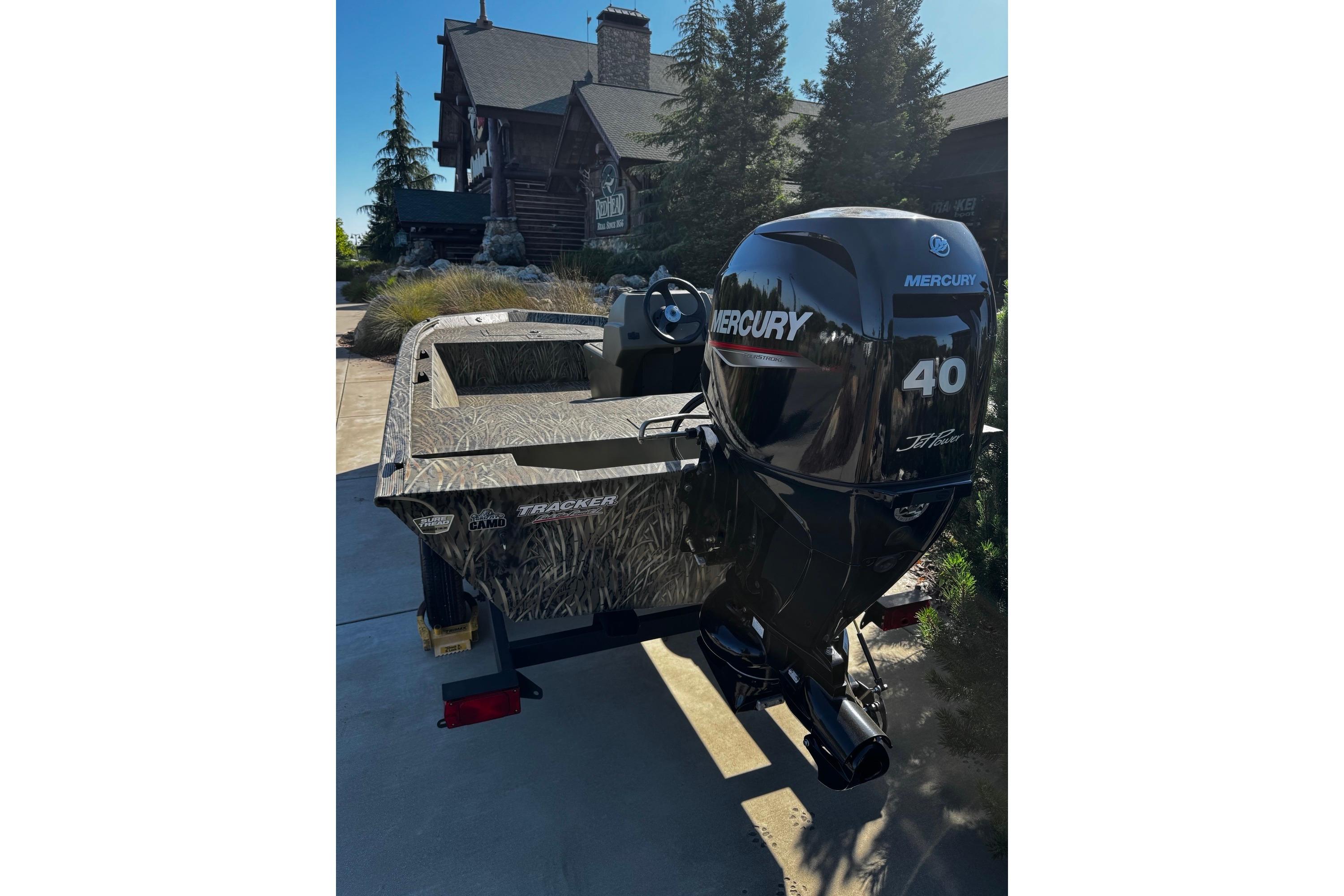 2026 Tracker Grizzly 1648 SC boat with Mercury 40 engine, parked near a rustic cabin.