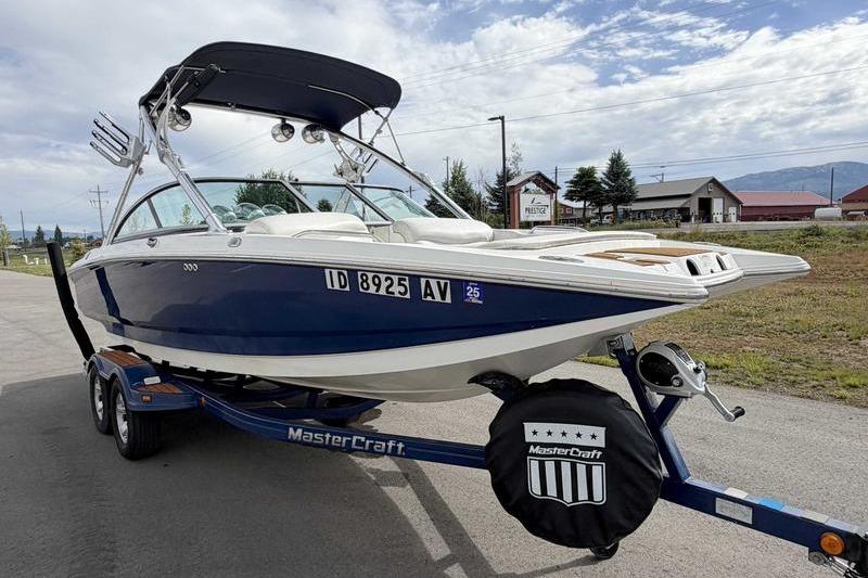 2004 MasterCraft XStar boat on trailer, blue and white, parked outdoors.