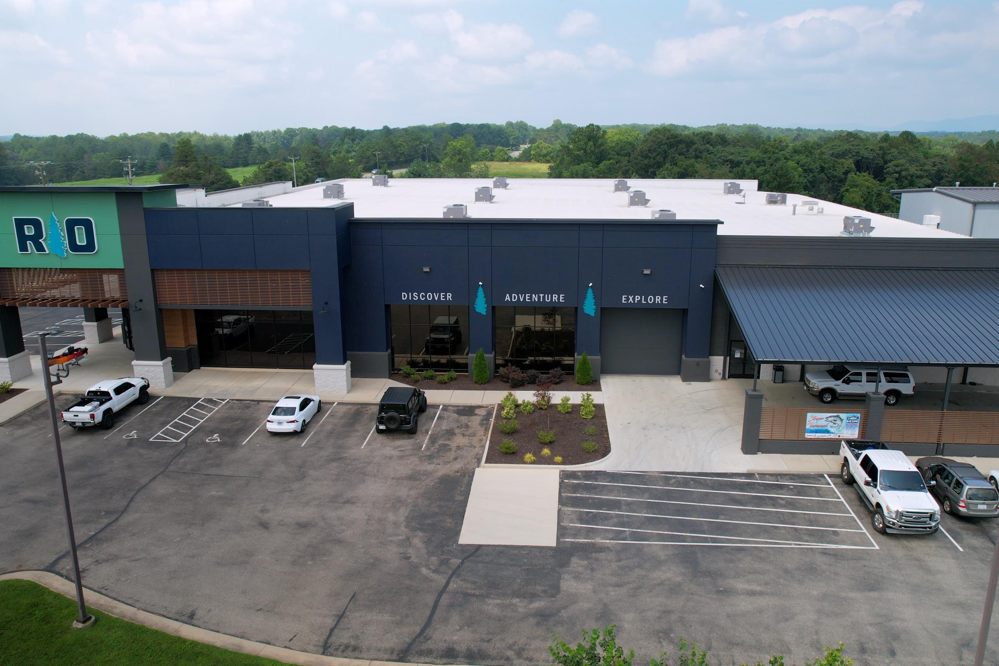 Aerial view of a modern commercial building with parking lot, surrounded by greenery.