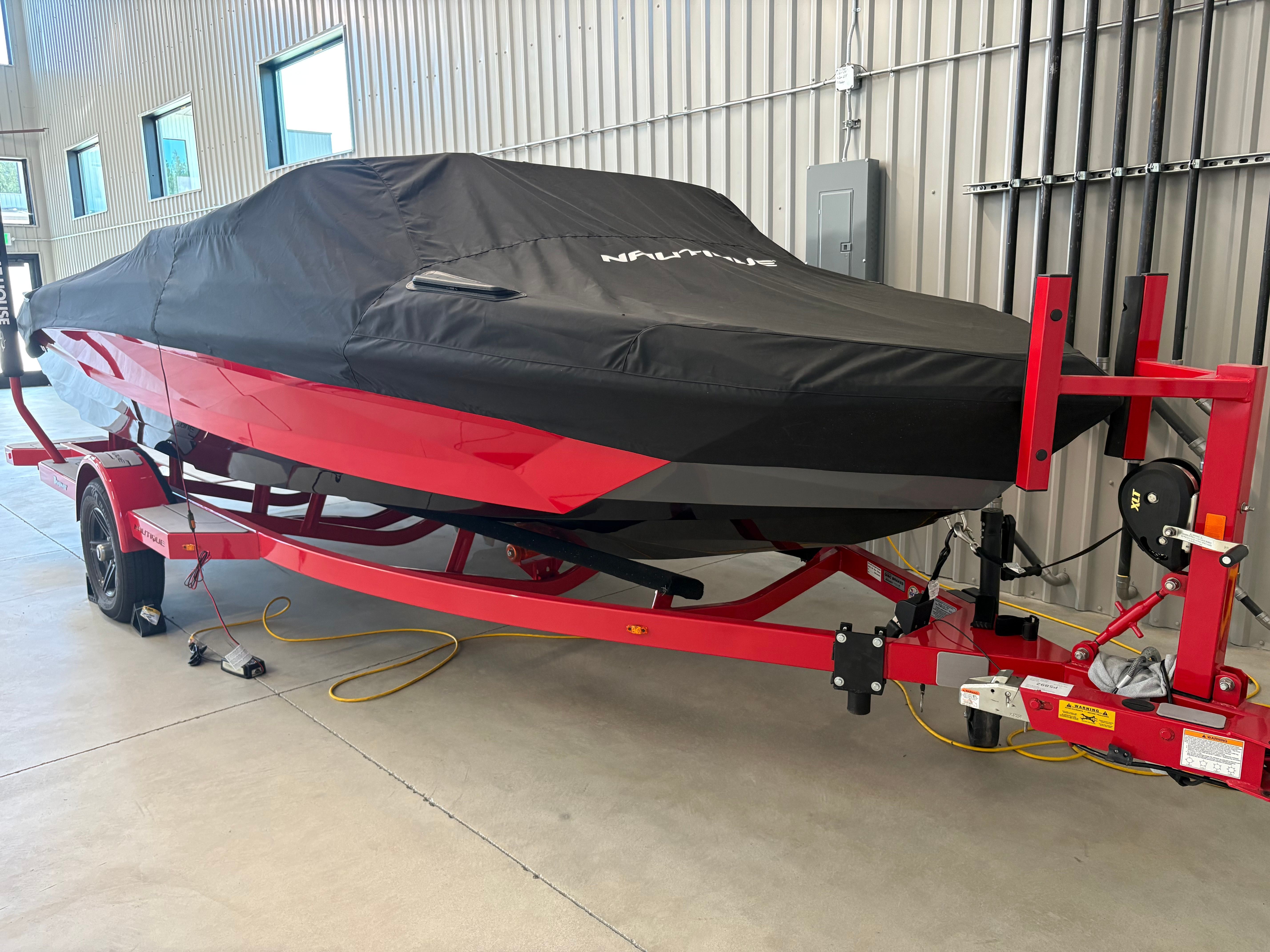 A red 2023 Ski Nautique boat is on a trailer in a warehouse.