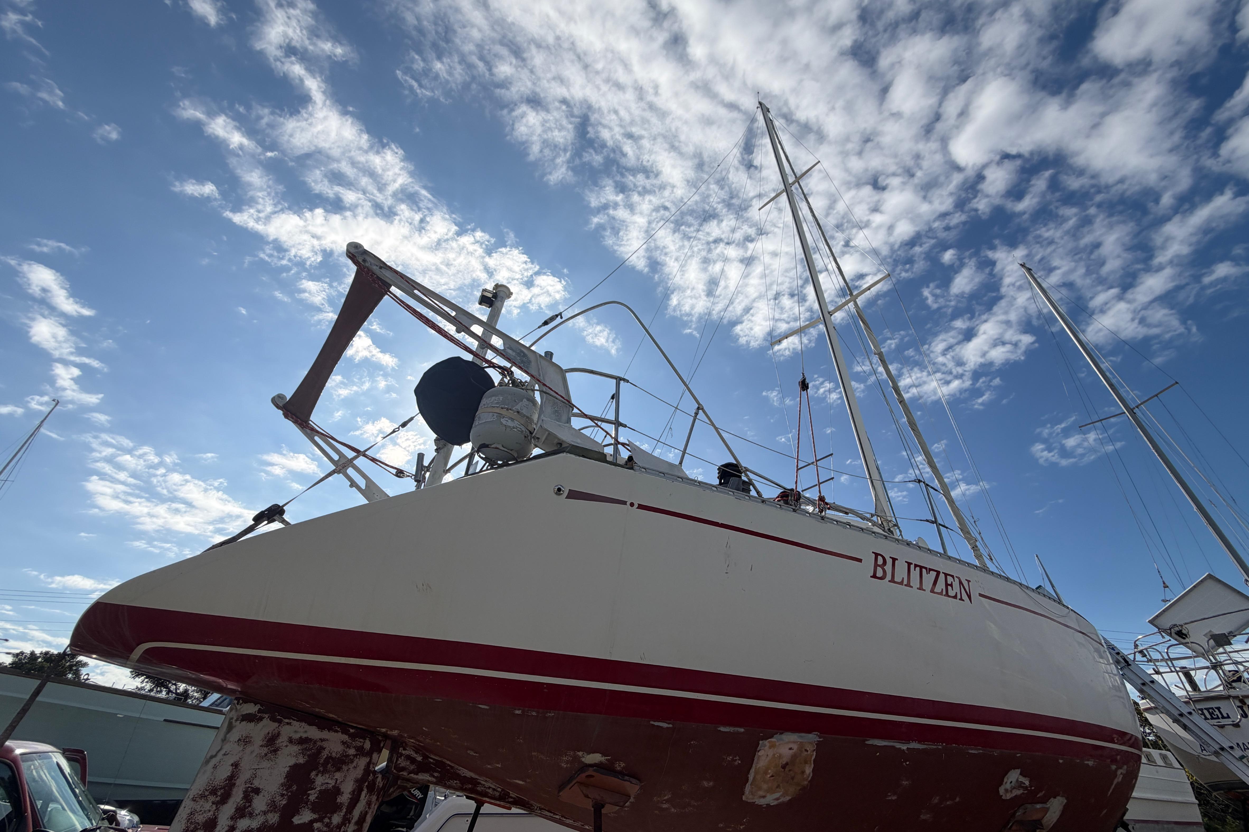 1983 Morgan Catilina sailboat named "Blitzen" under a bright blue sky with clouds.