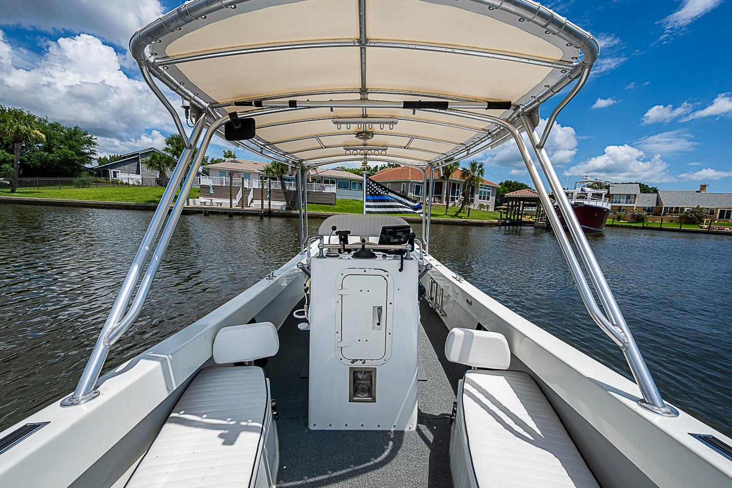 Custom 1969 boat with canopy on a calm river, surrounded by waterfront homes.