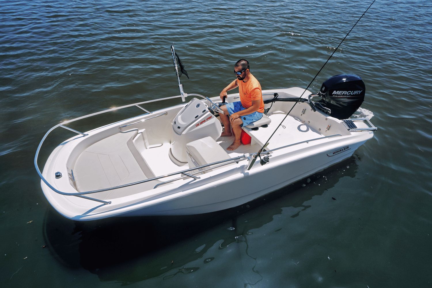A man navigates a Boston Whaler 130 Super Sport boat on calm water.