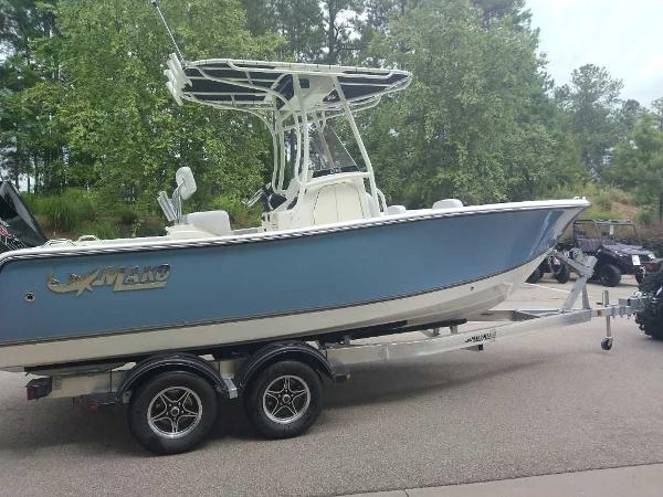 2023 Mako 214 CC boat on a trailer in a wooded area.