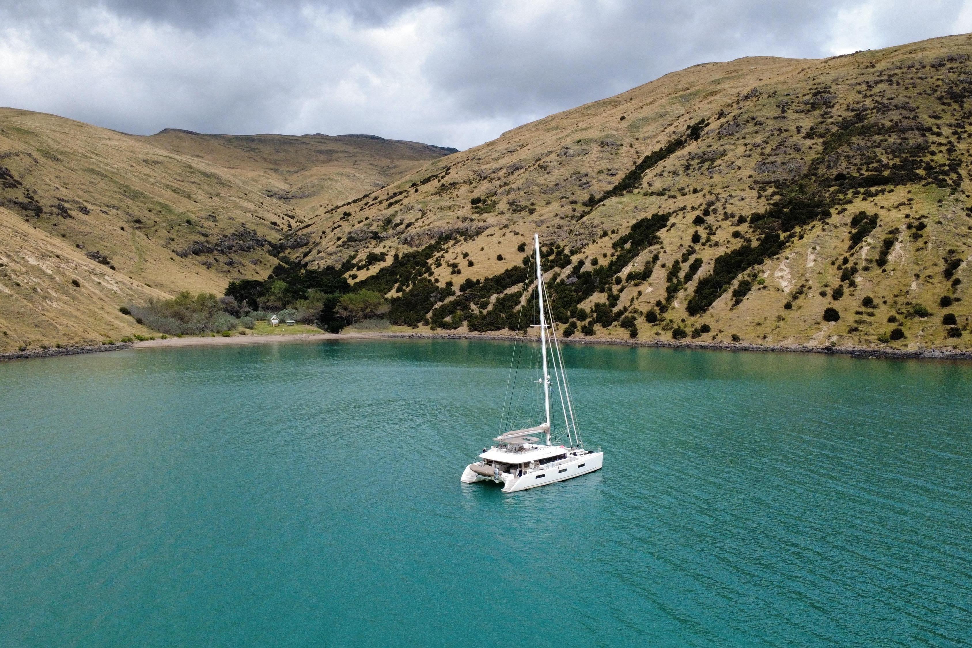 Lagoon 620 catamaran sailing in a serene bay surrounded by lush hills, 2019 model.