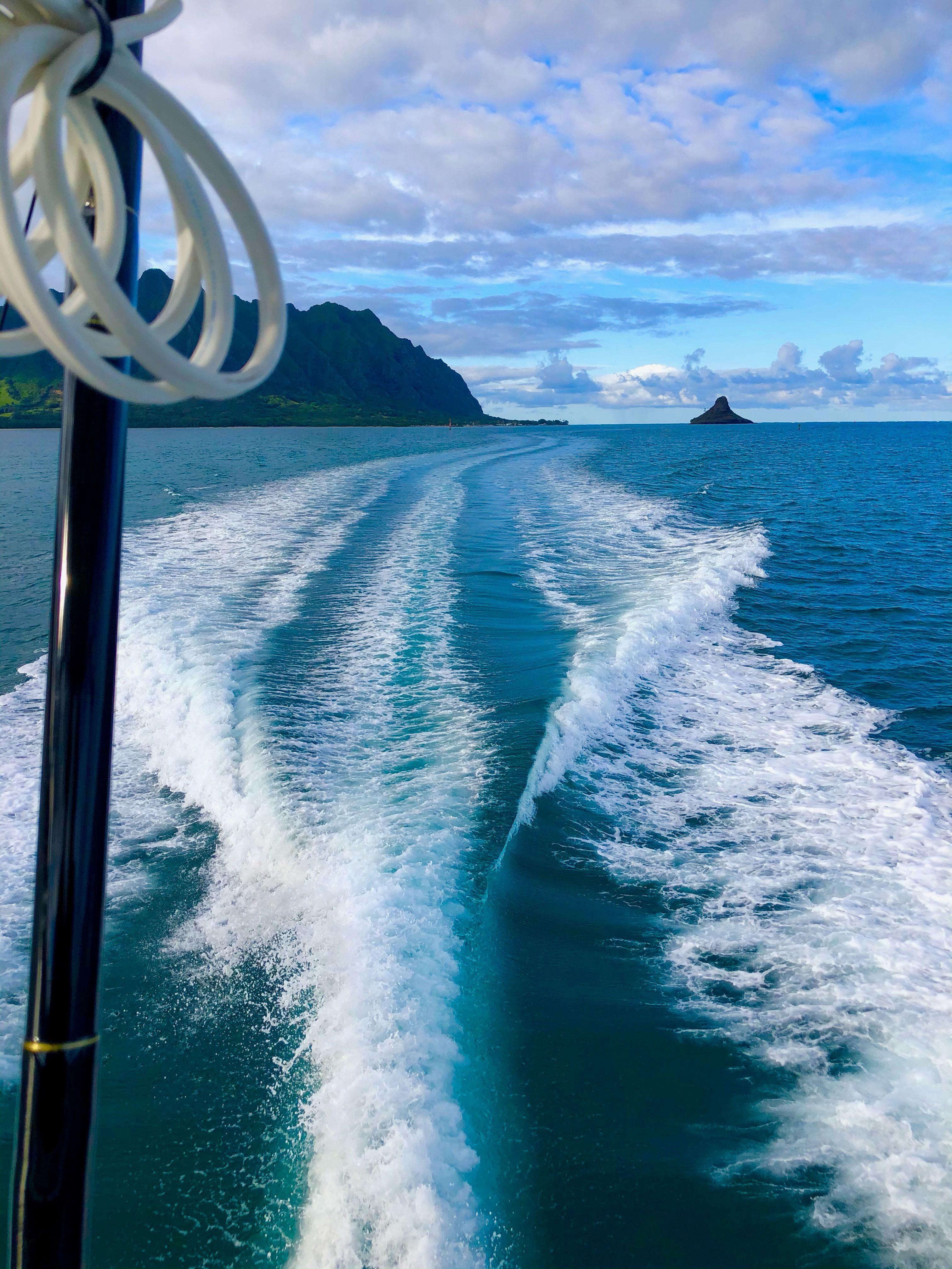 A boat leaves a wake in the blue water under a cloudy sky.