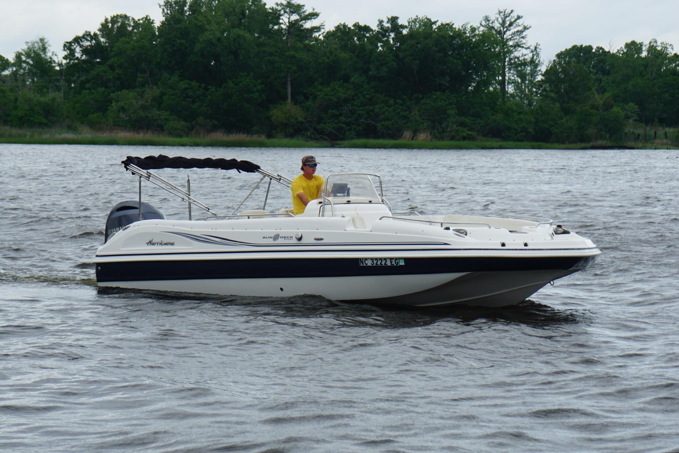 2015 Hurricane SunDeck Sport 231 OB boat cruising on a lake with lush green background.