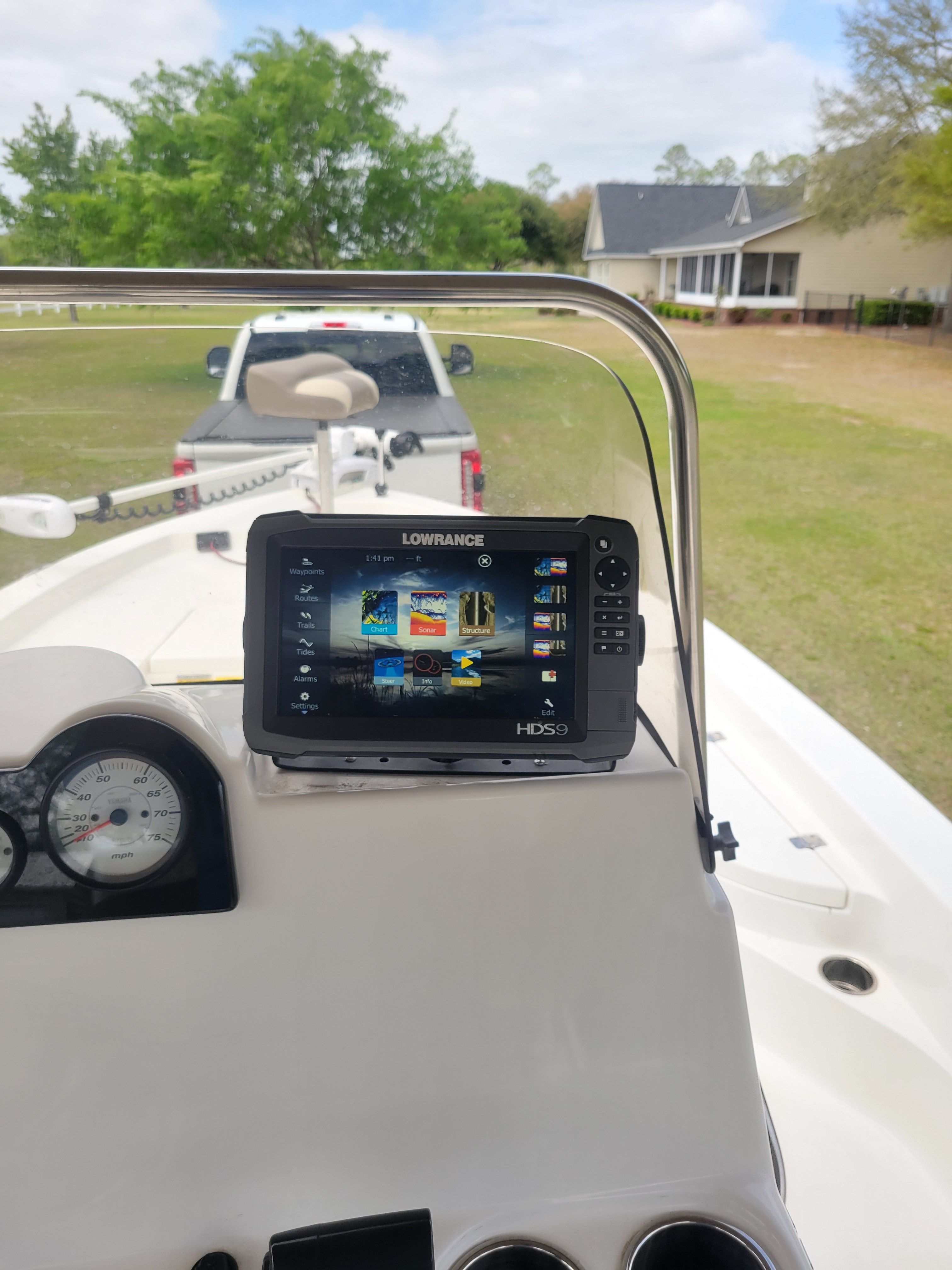 A boat with a navigation system, parked on a trailer in front of a house.