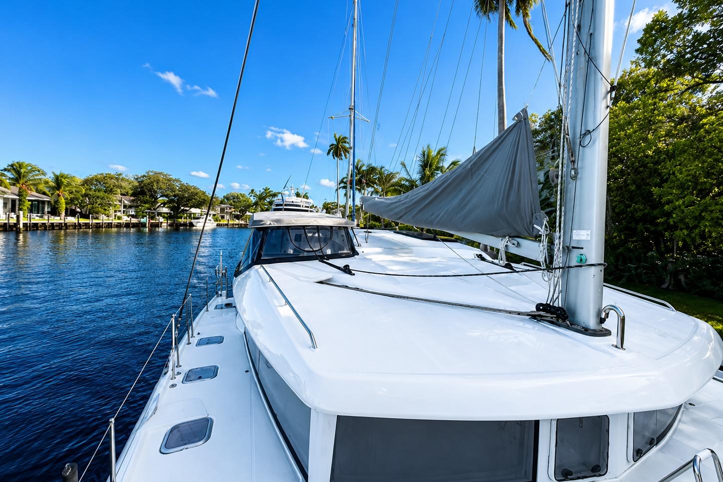 2010 Lagoon 421 catamaran sailing on a serene waterway with palm trees.