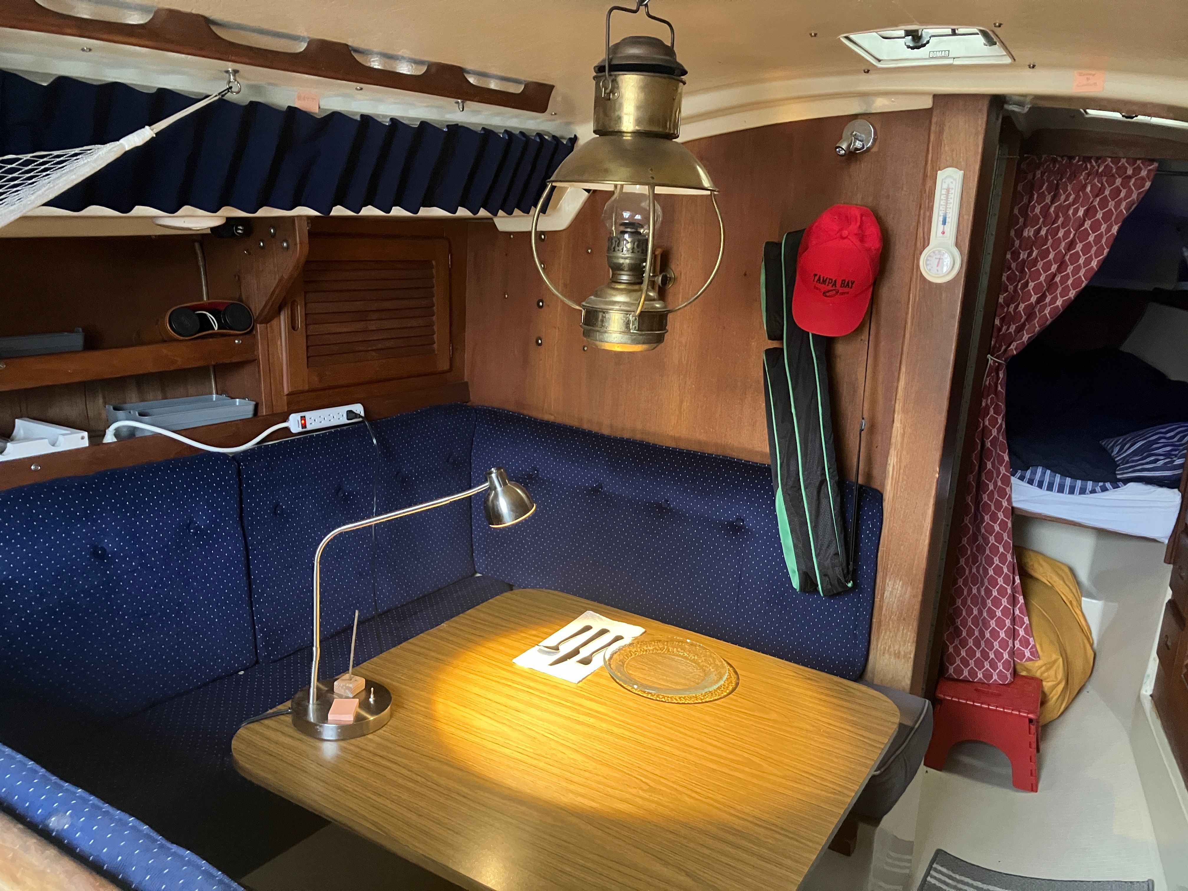 Cozy interior of a 1984 Catalina 30 with wooden table, blue cushioned seating, and brass lamp.