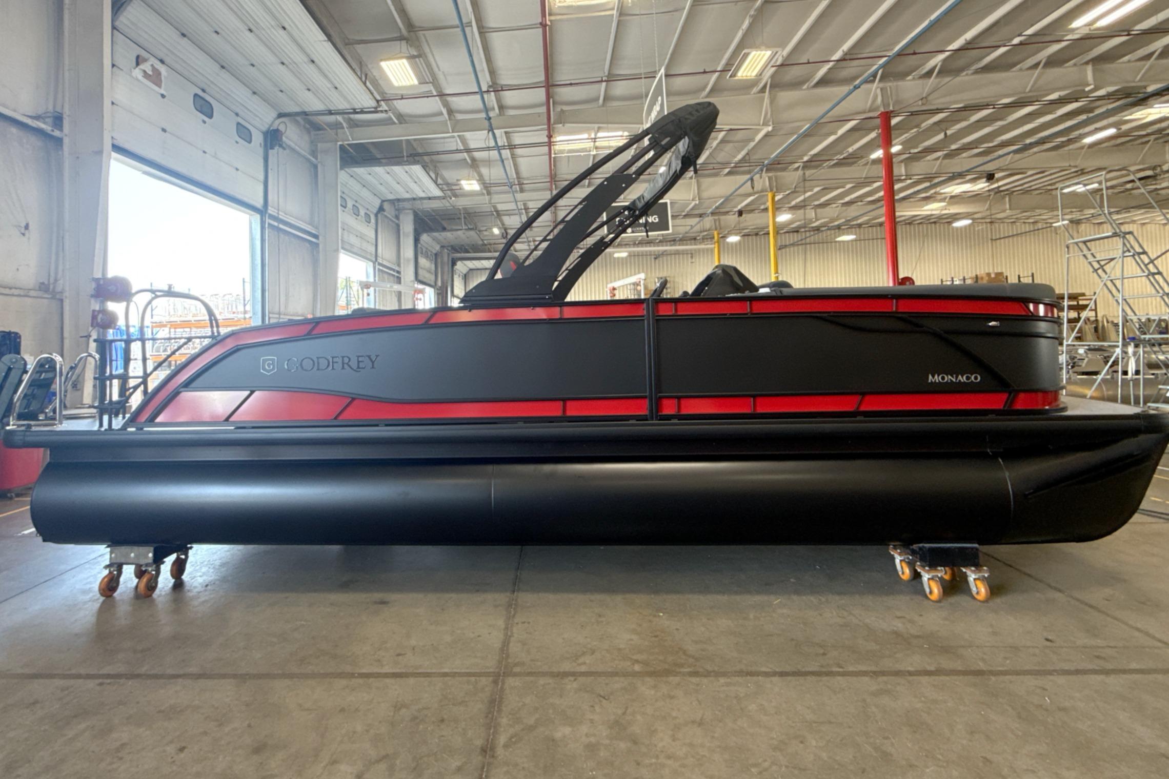 2027 Godfrey Monaco 25' Tritoon in warehouse, sleek black and red design.