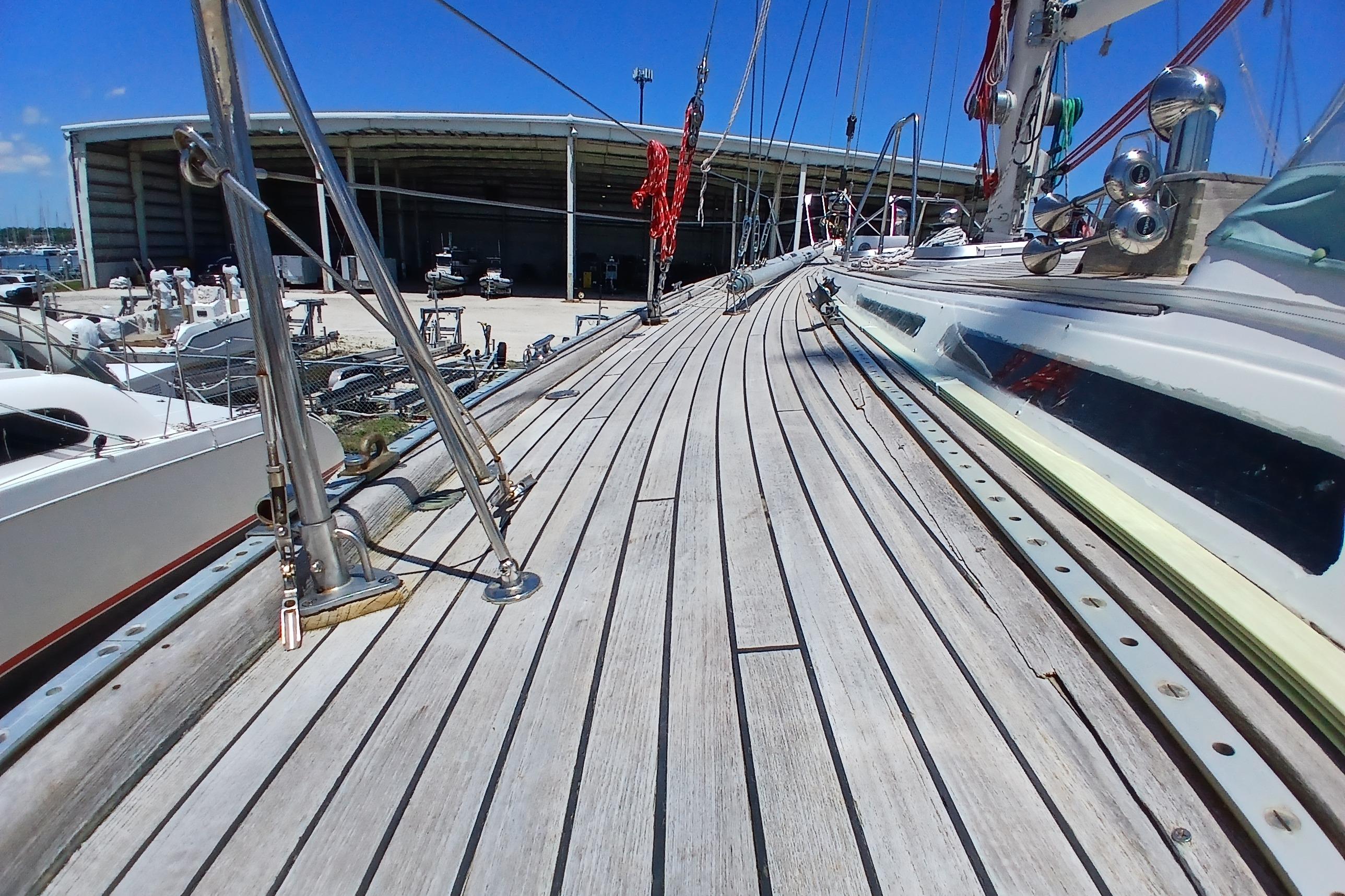 Deck view of 1981 Kaufman Skye 51 sailboat in marina, showcasing wooden planks and rigging.