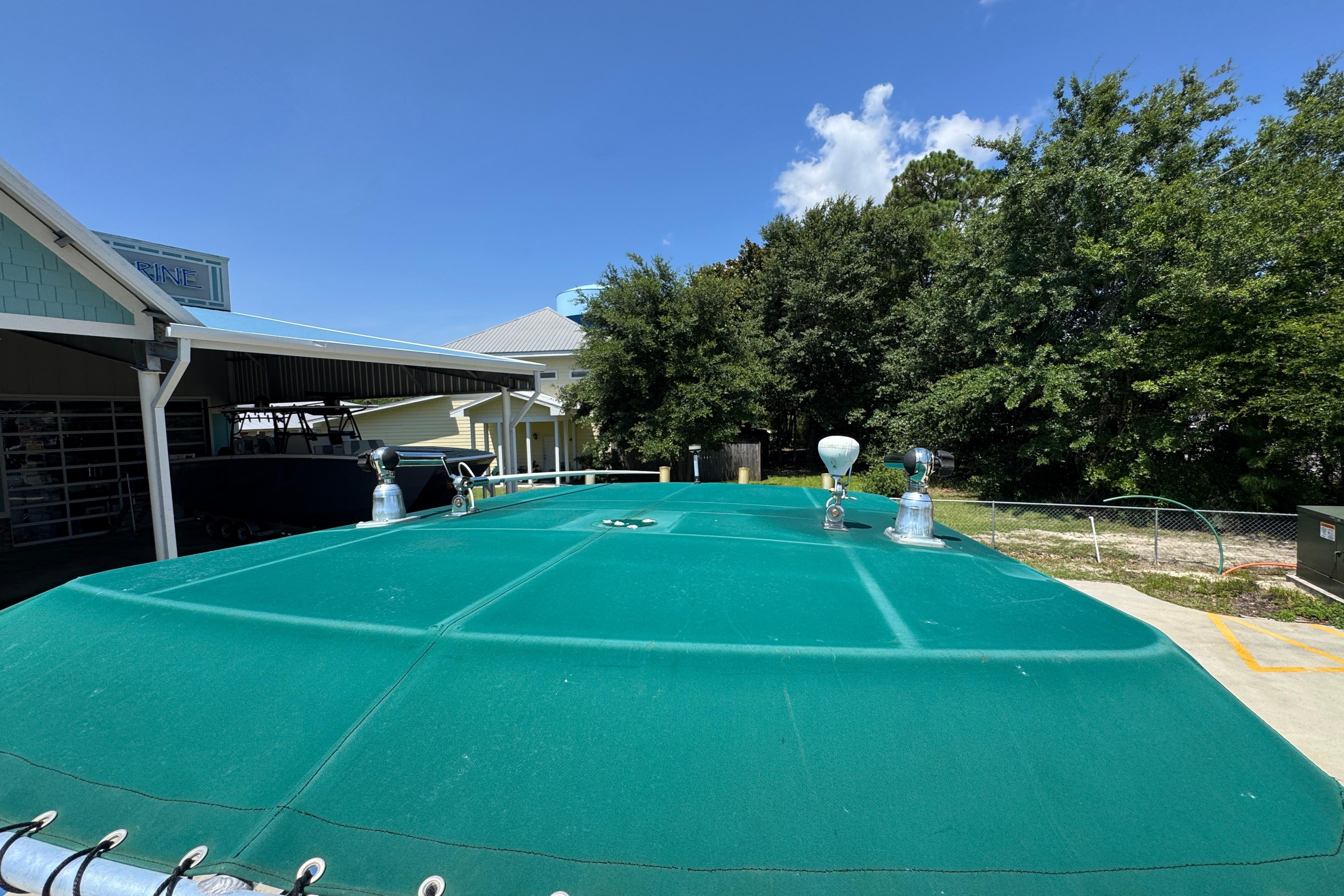 2000 Stamas 250 Tarpon boat with green cover, parked outdoors under clear blue sky.