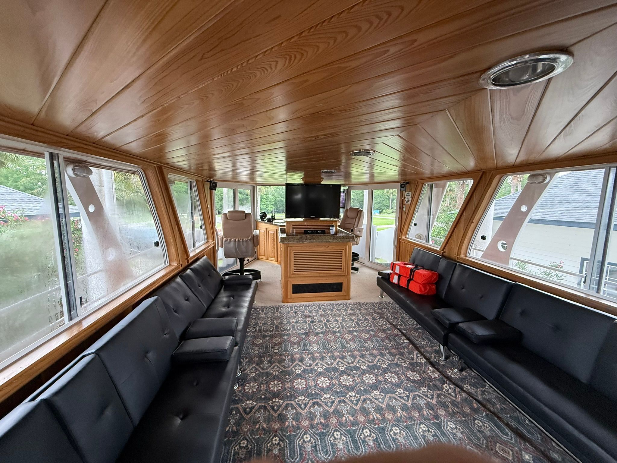 Interior of a houseboat with wooden walls, black sofas, and a television.